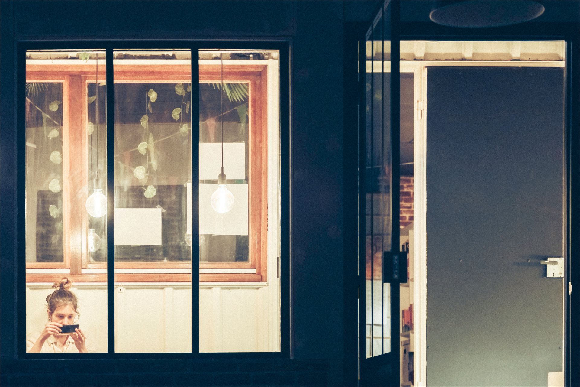 A person looking at their phone in a window at night. Lit room, open door to the right.
