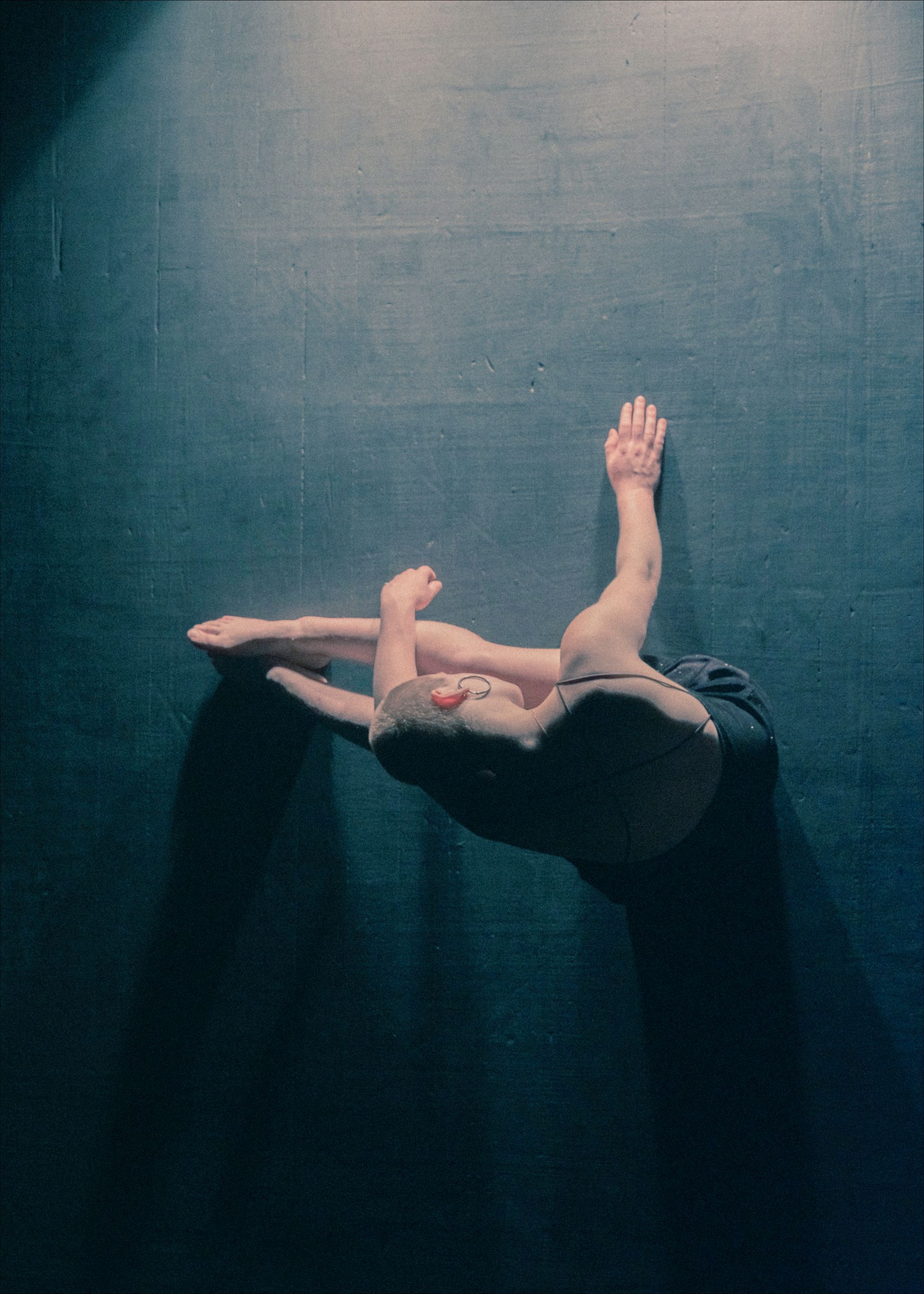 Dancer on a dark stage, arm raised, body curved. Overhead view.
