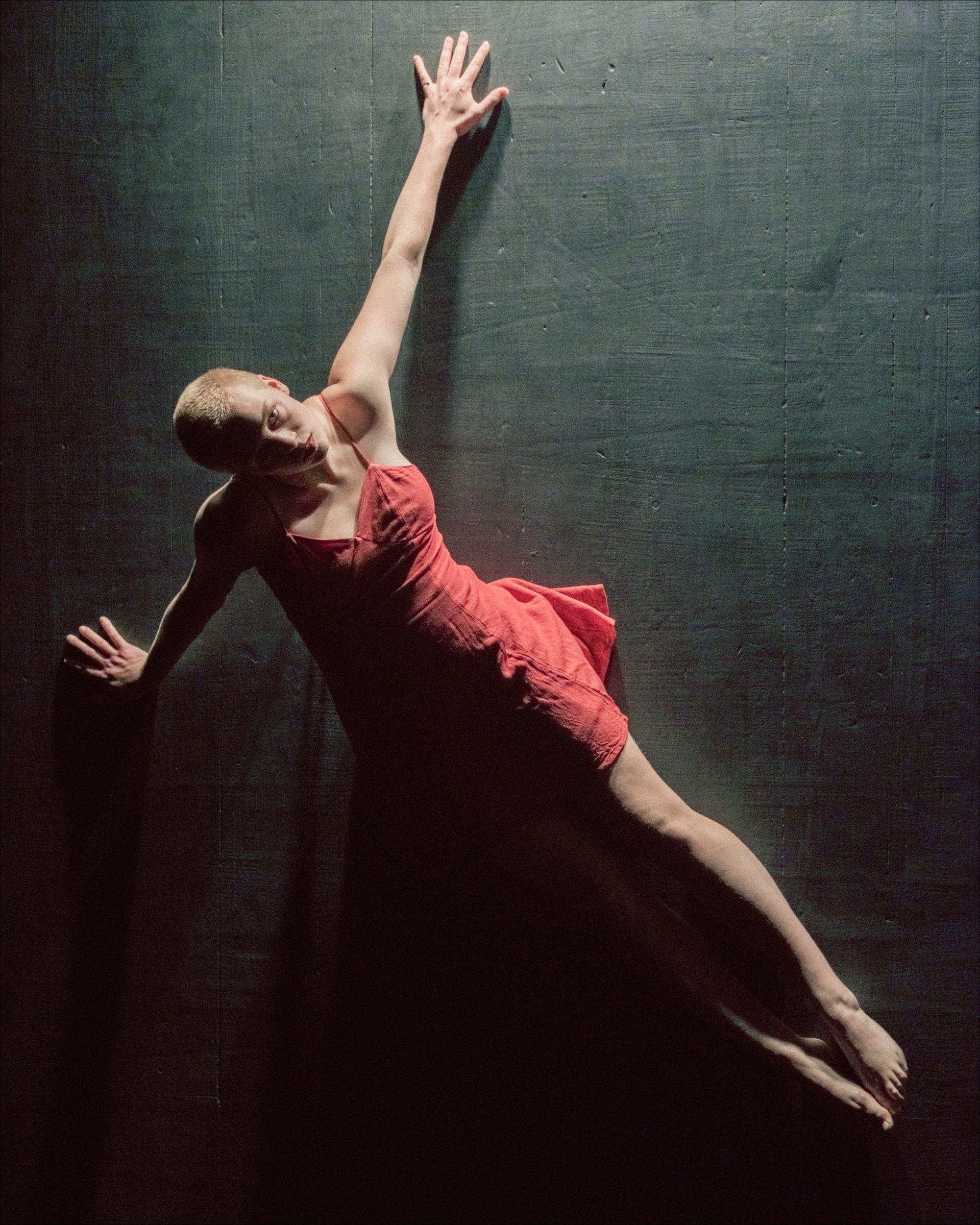 Dancer in a red dress, mid-air, arm extended. Dark background, possibly a stage.