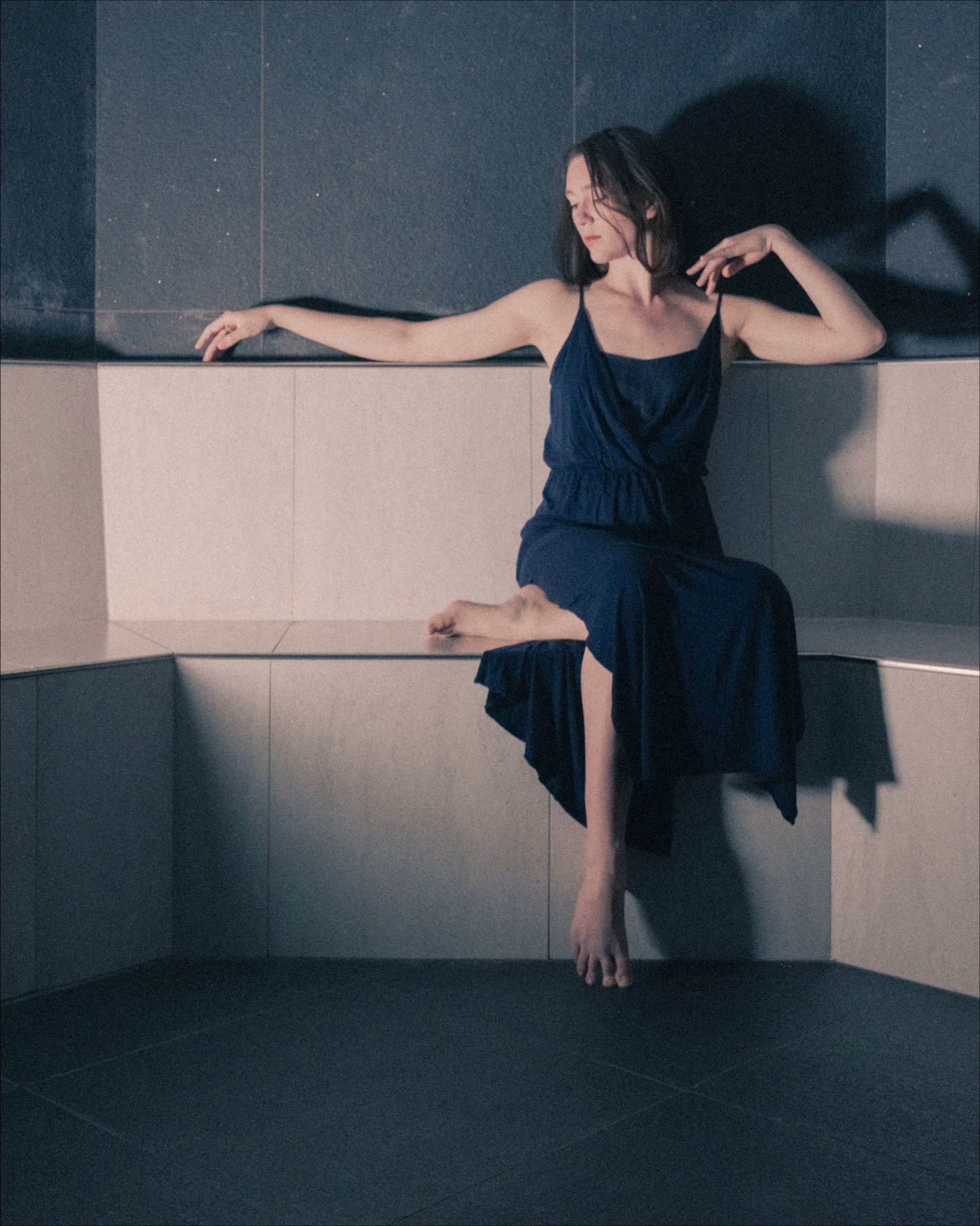Woman in blue dress sitting on stone ledge, arm outstretched.