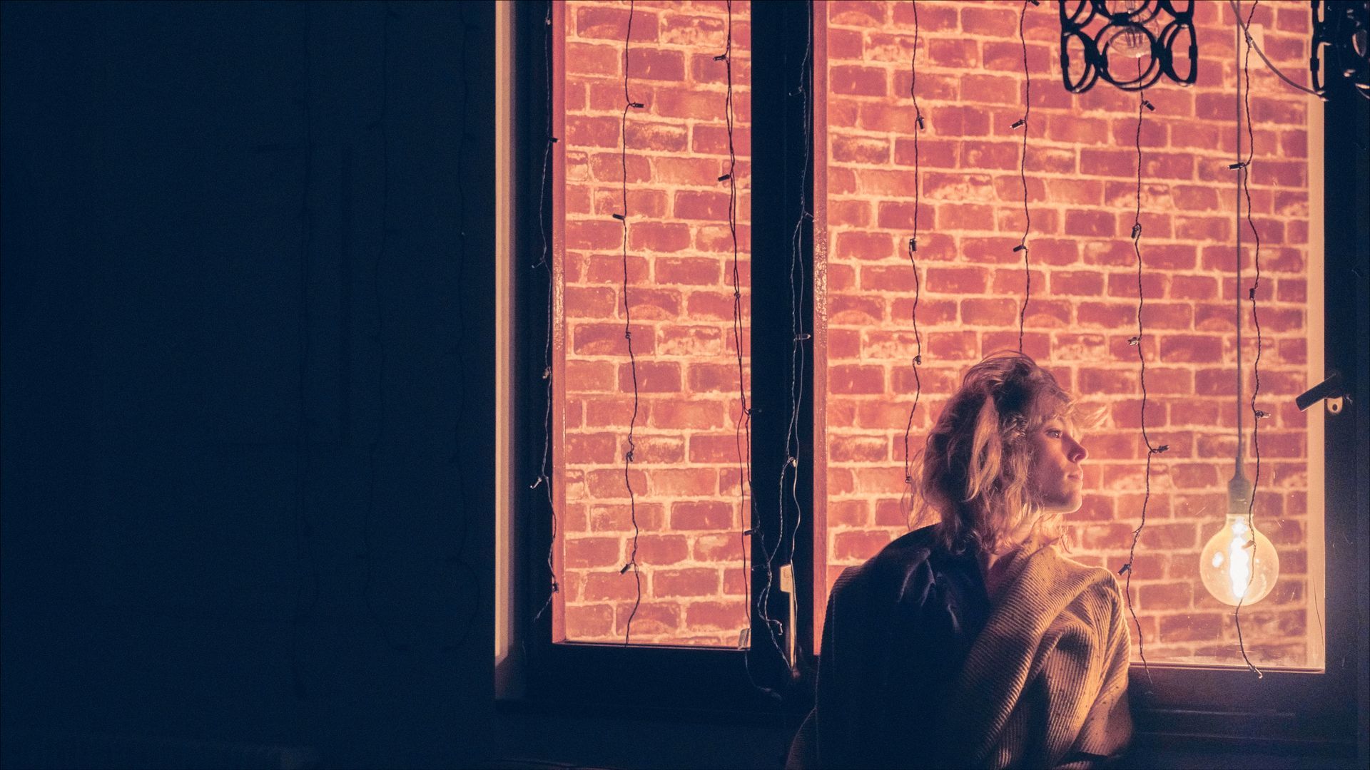 Person looking out a window at a brick wall. Warm orange light illuminates the scene.