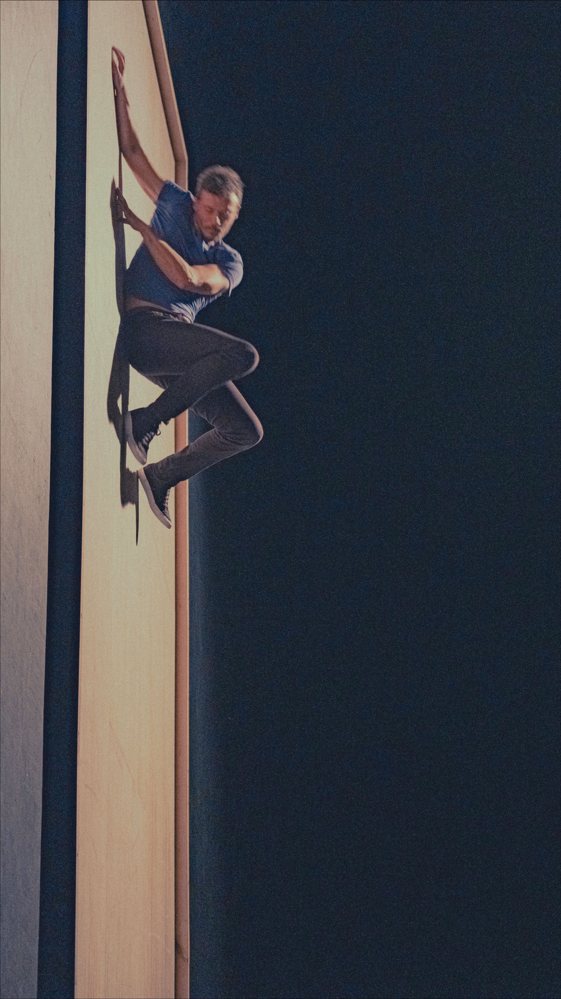 Man clinging to the side of a tall building, dark background.