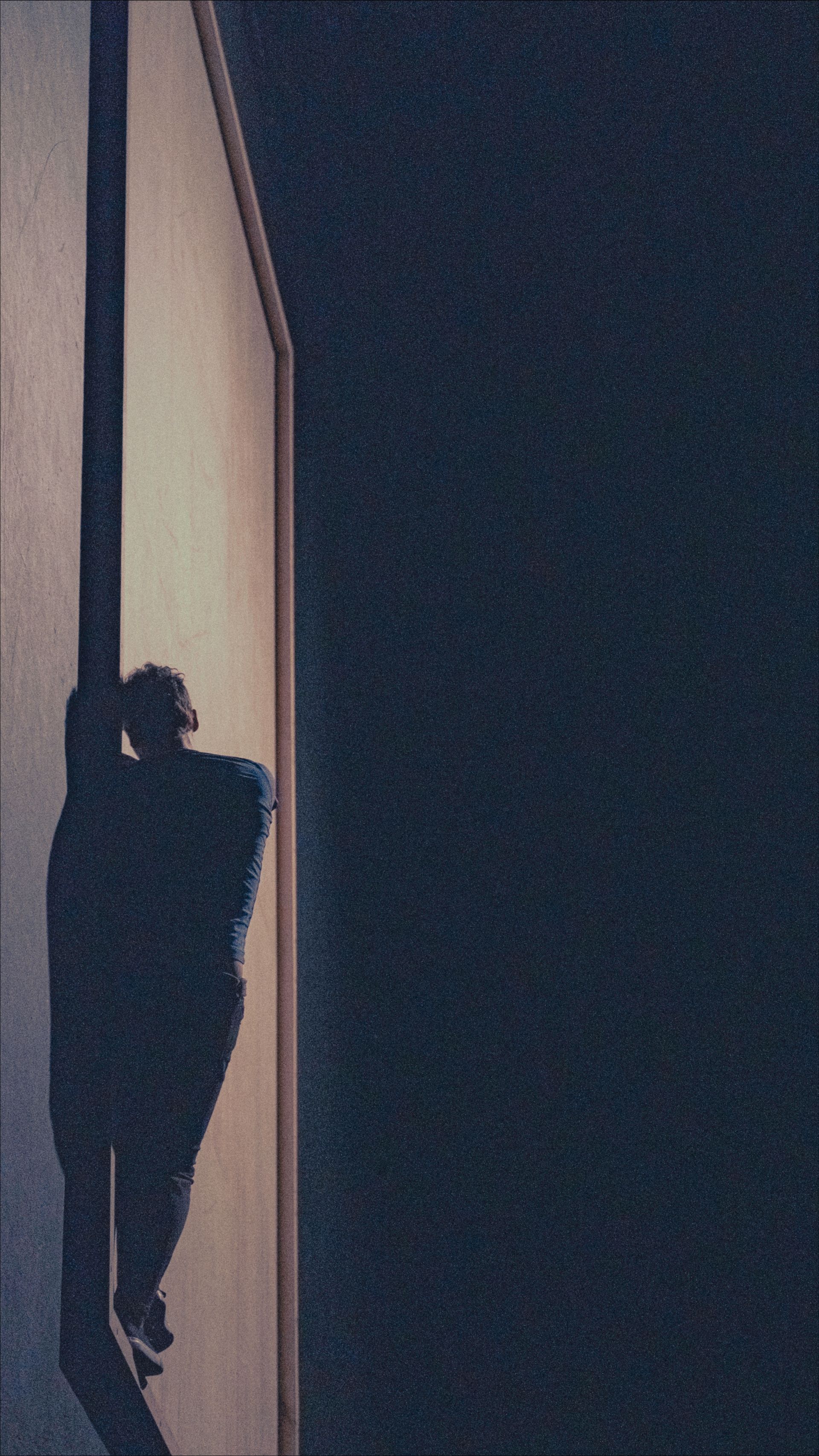 Silhouette of a person clinging to a tall, vertical surface against a dark background.
