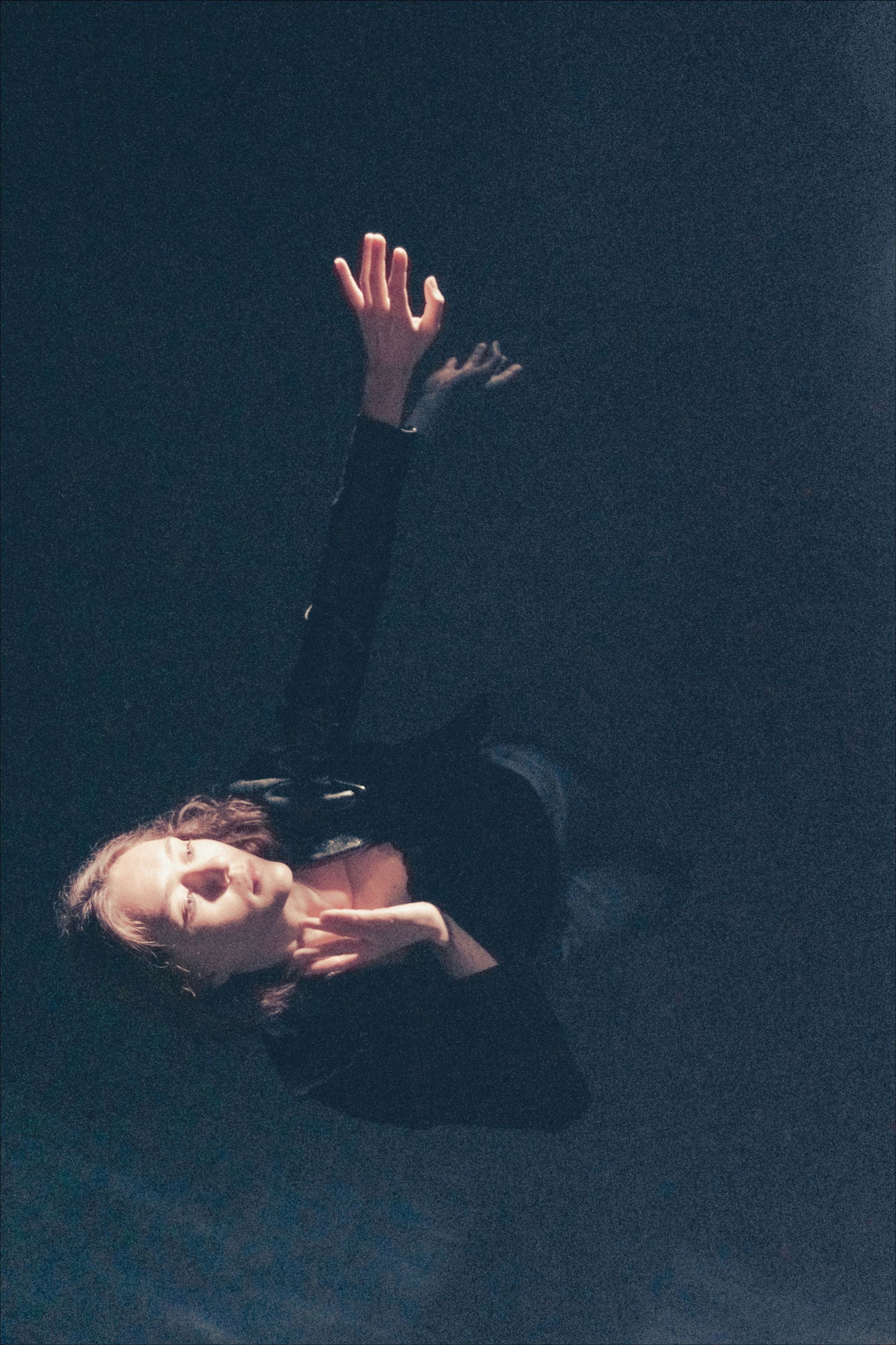 Person floating in dark space, arms outstretched, face tilted up.