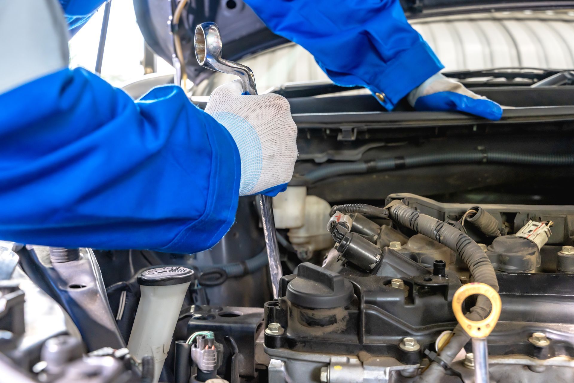 Mechanic in blue overalls working on a car engine with a wrench | Torque Automotive
