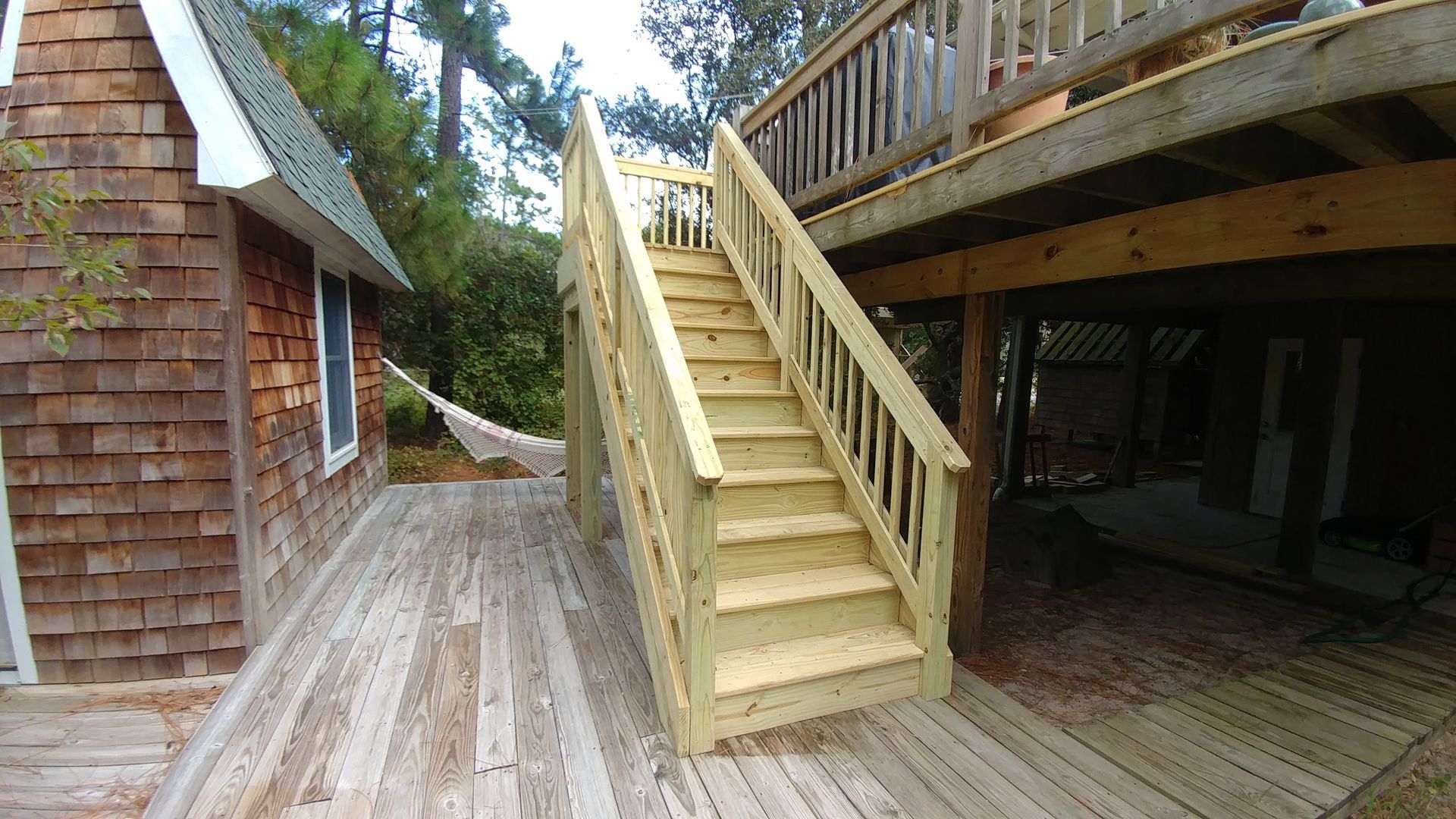 Wooden outdoor staircase leads to a deck, attached to a brown shingled house.
