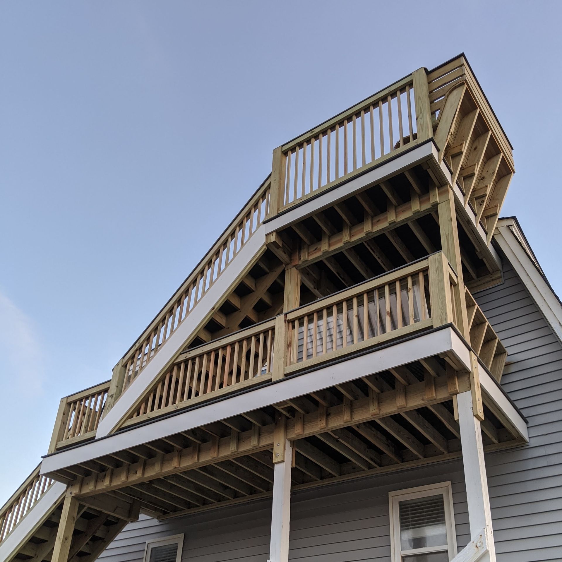 Wooden multi-level deck with stairs against a gray house, blue sky above.