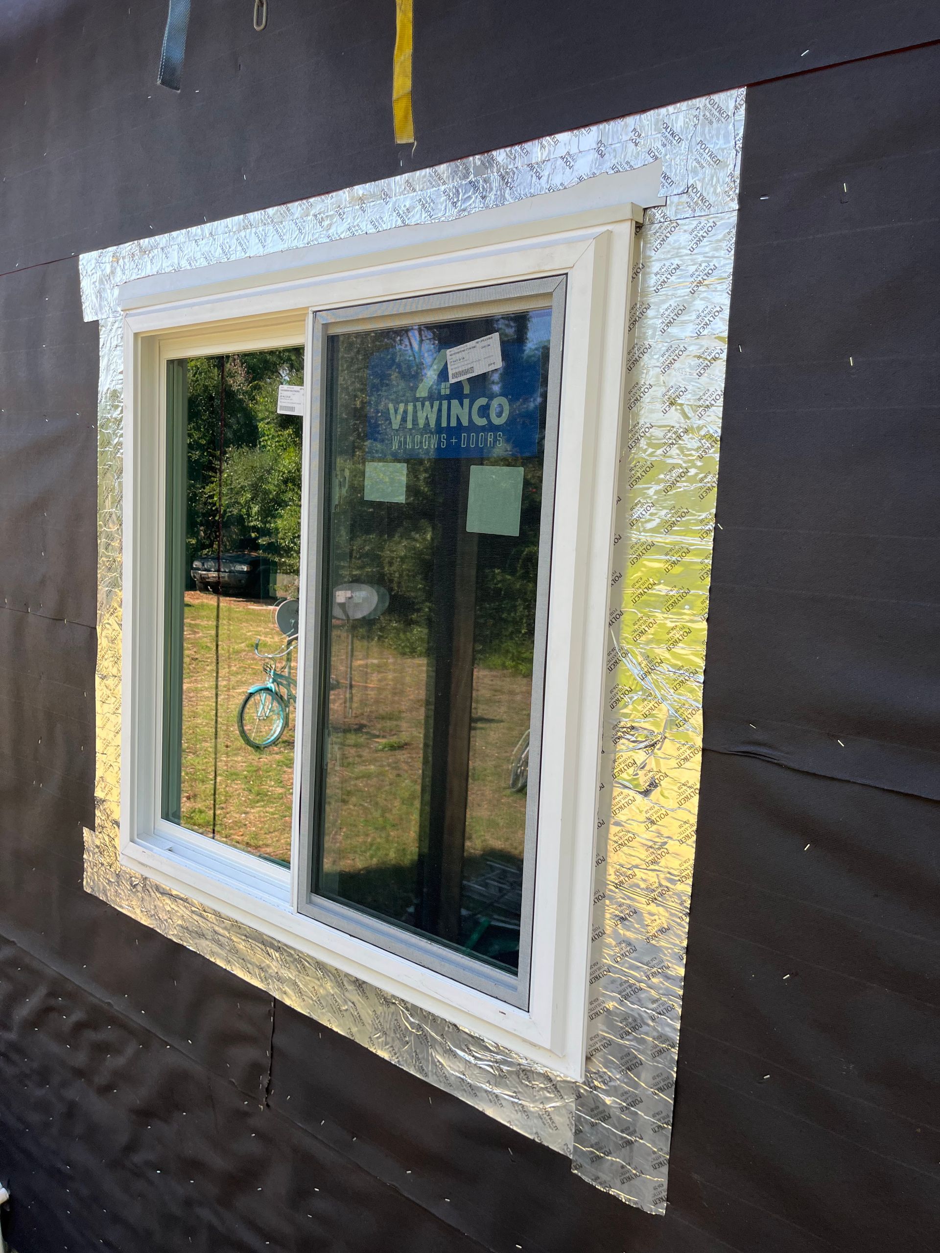 White window frame with silver flashing on dark siding, exterior view.