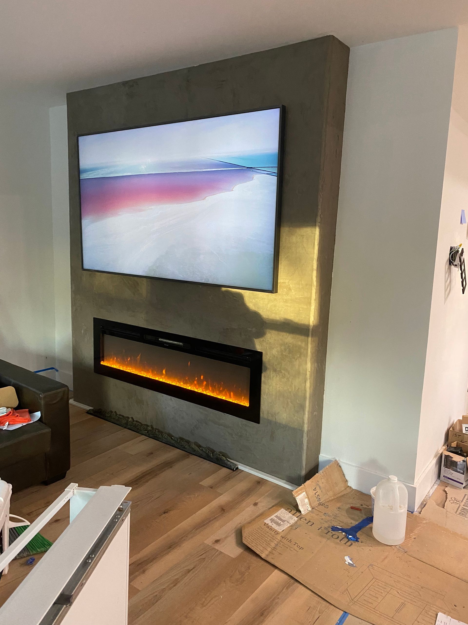 Gray stucco wall with mounted TV and fireplace; light wood floor.
