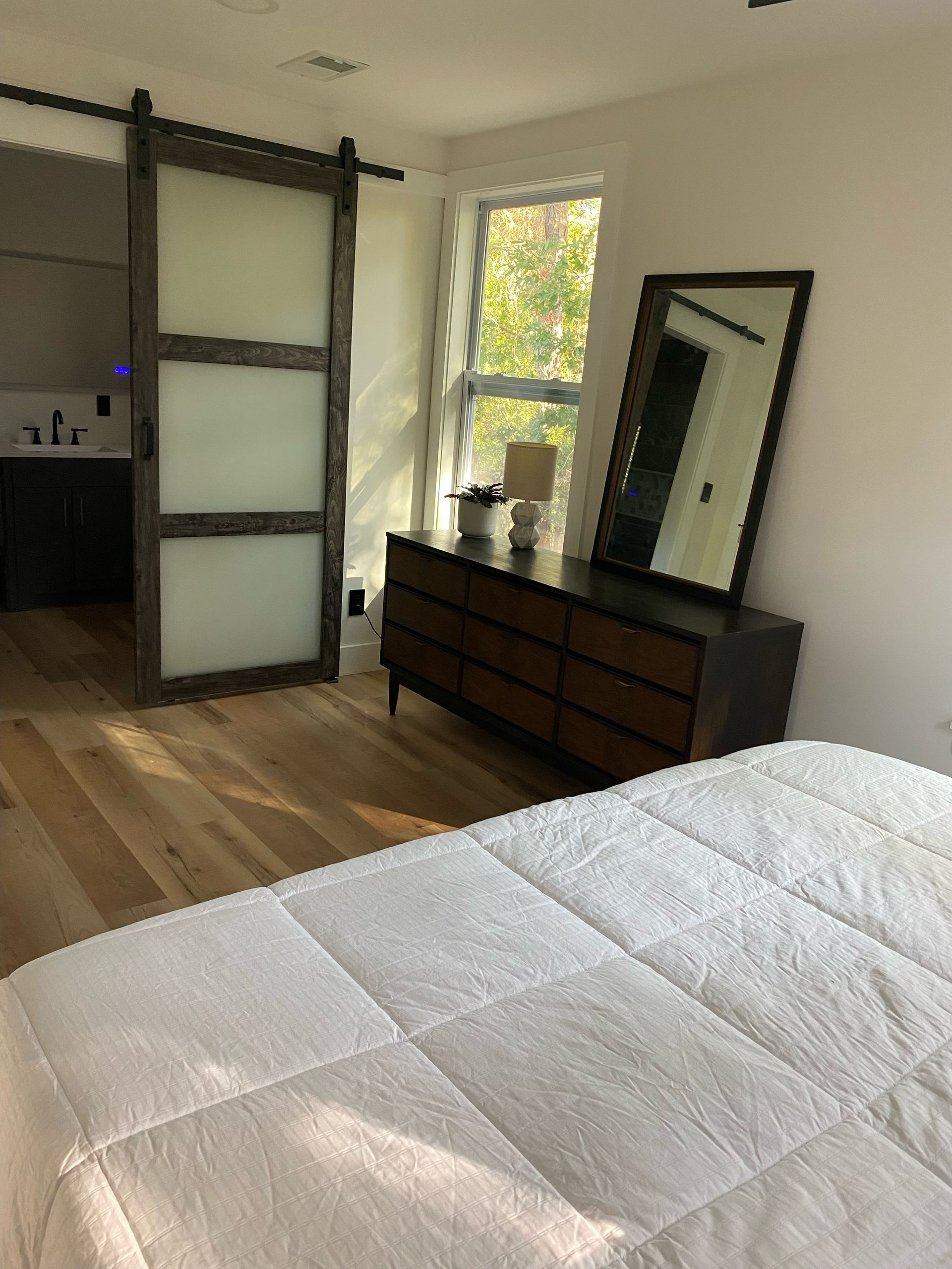 Bedroom with a dark wood dresser, mirror, sliding door, and bed with white bedding.