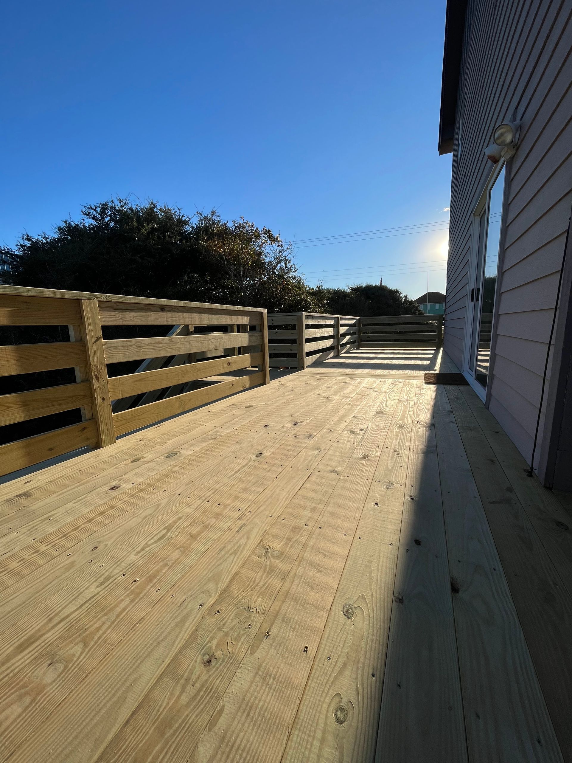 Wooden deck with a slatted railing and partial view of a building exterior, blue sky.