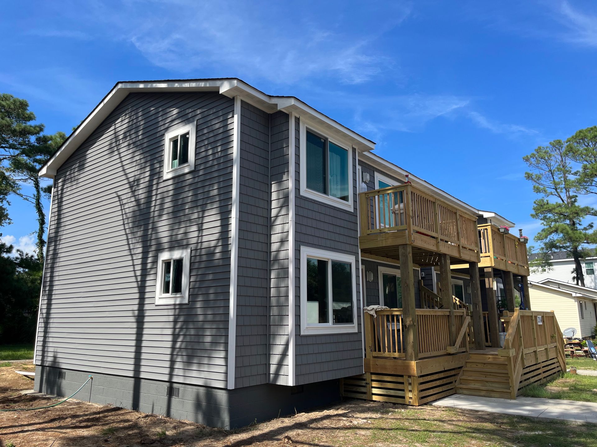 Gray two-story house with white window frames and a wooden deck. Sunny day, blue sky.