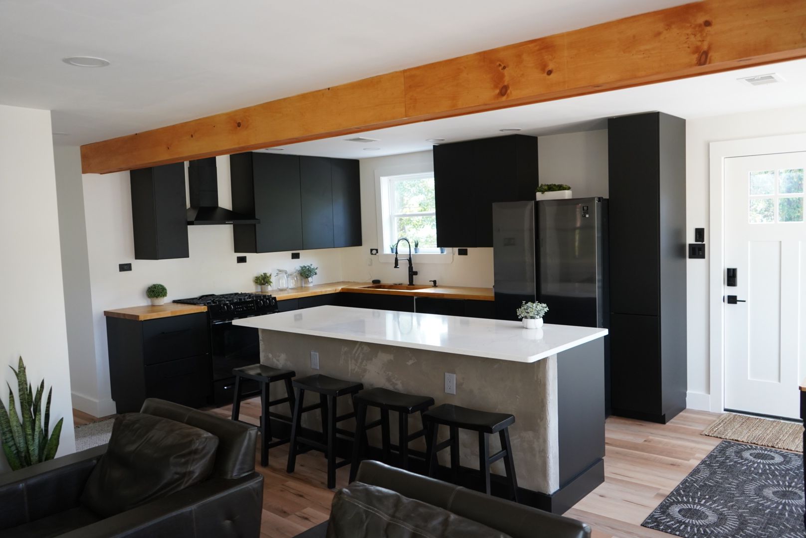 Modern kitchen with black cabinets, wooden beam, white island, and stools.