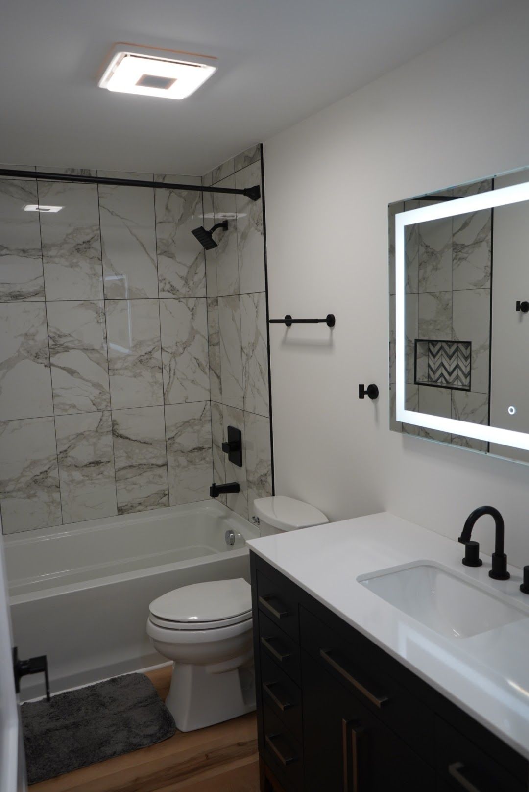 Modern bathroom with marble tile, black fixtures, and a vanity with a lit mirror.