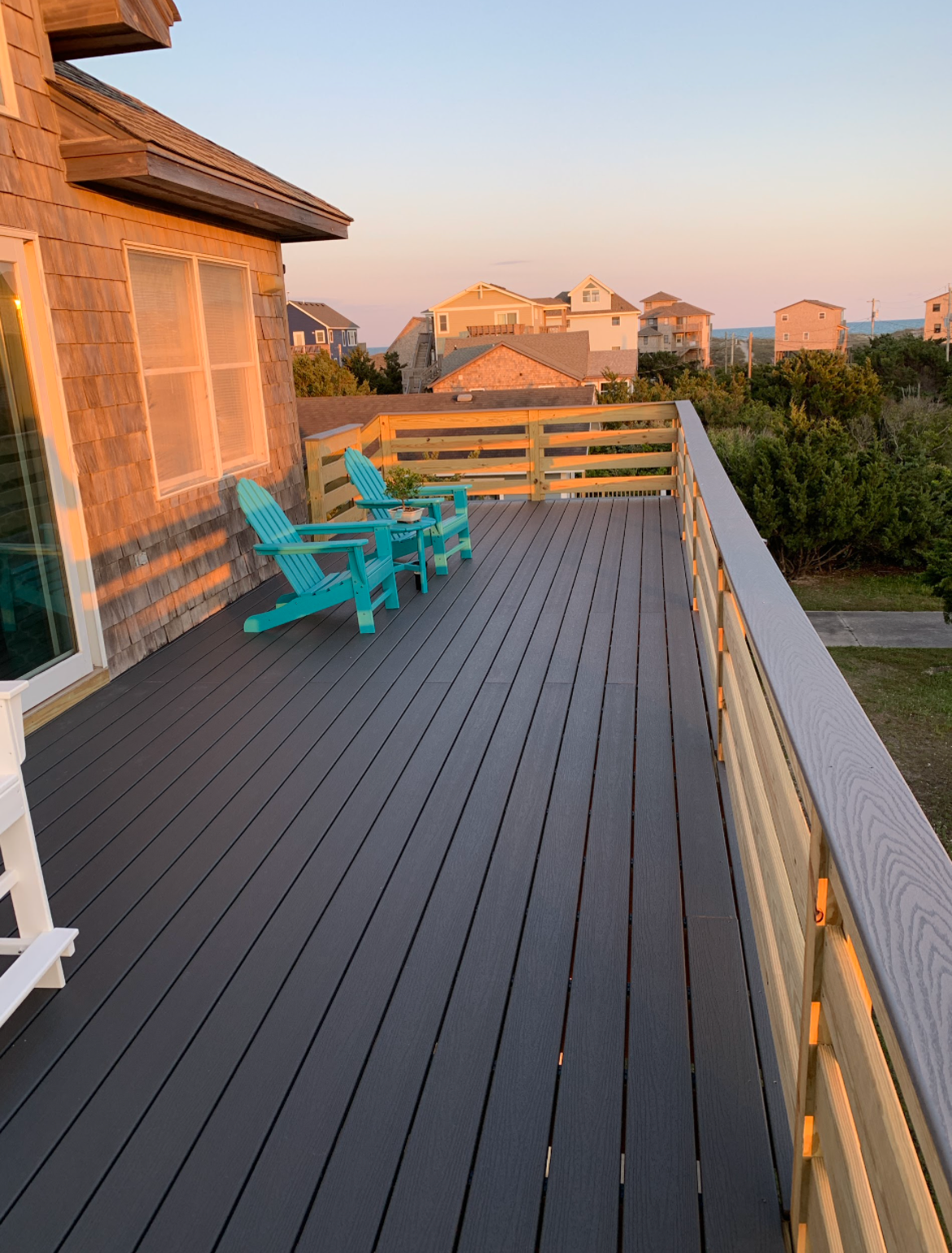 A wooden deck with teal chairs at sunset, overlooking a neighborhood.