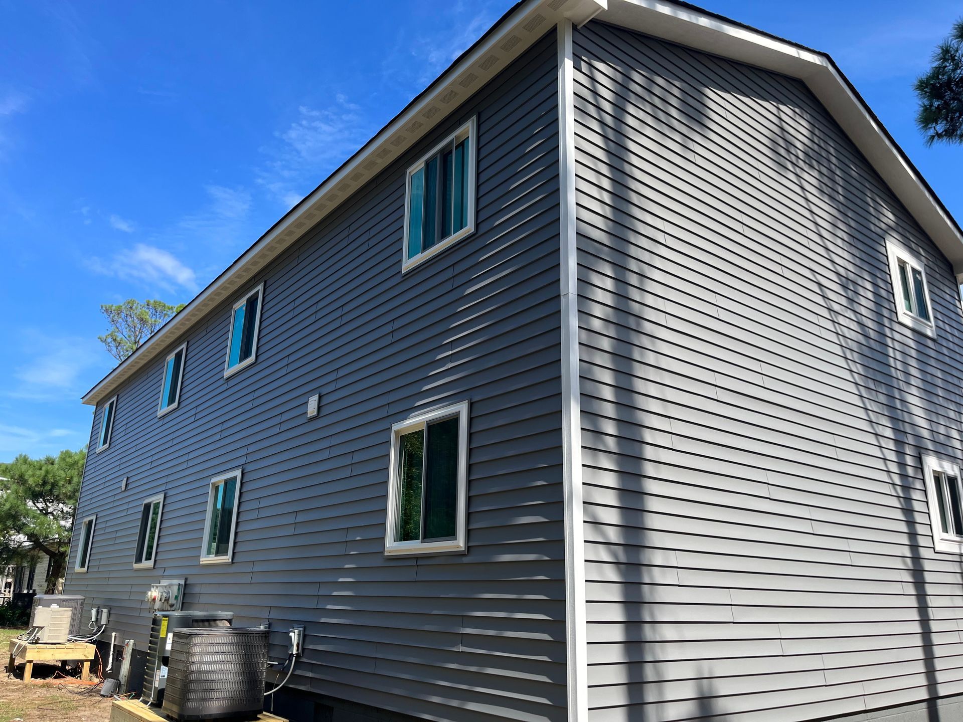 Two-story gray building with white trim and windows against a blue sky.