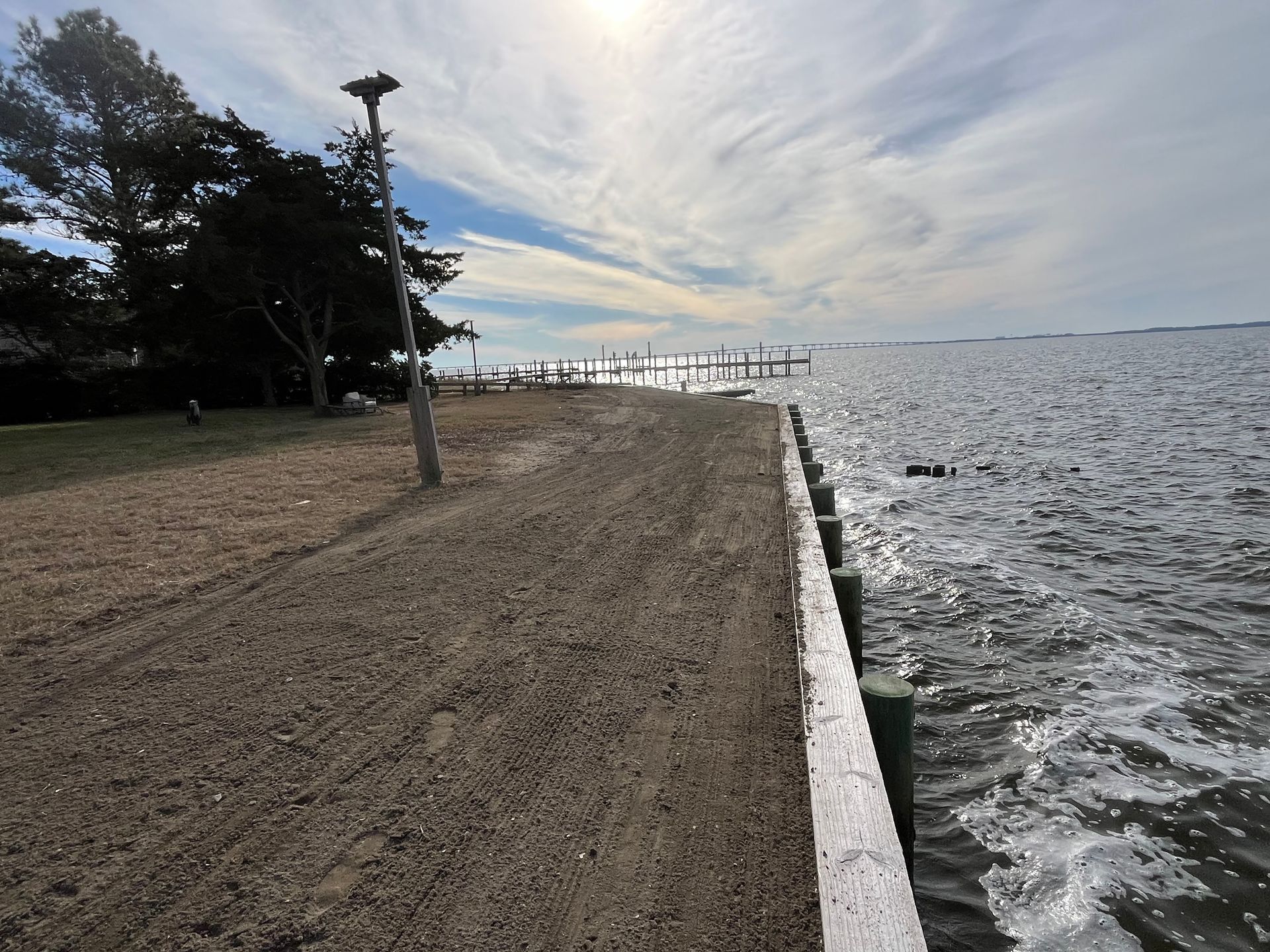 Shoreline with a gravel path, water, sky with clouds, and a lamppost.