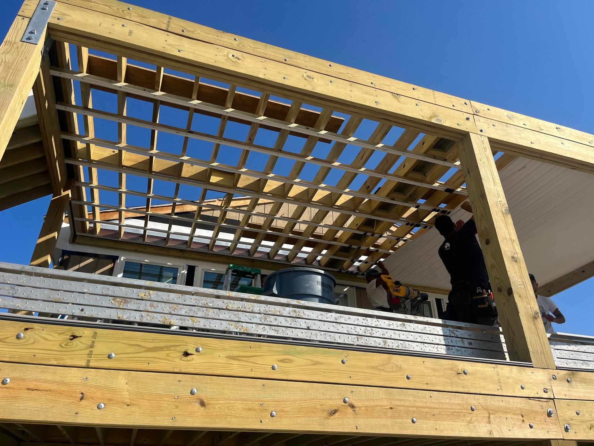 Construction worker framing a wooden pergola over a deck with a blue sky backdrop.