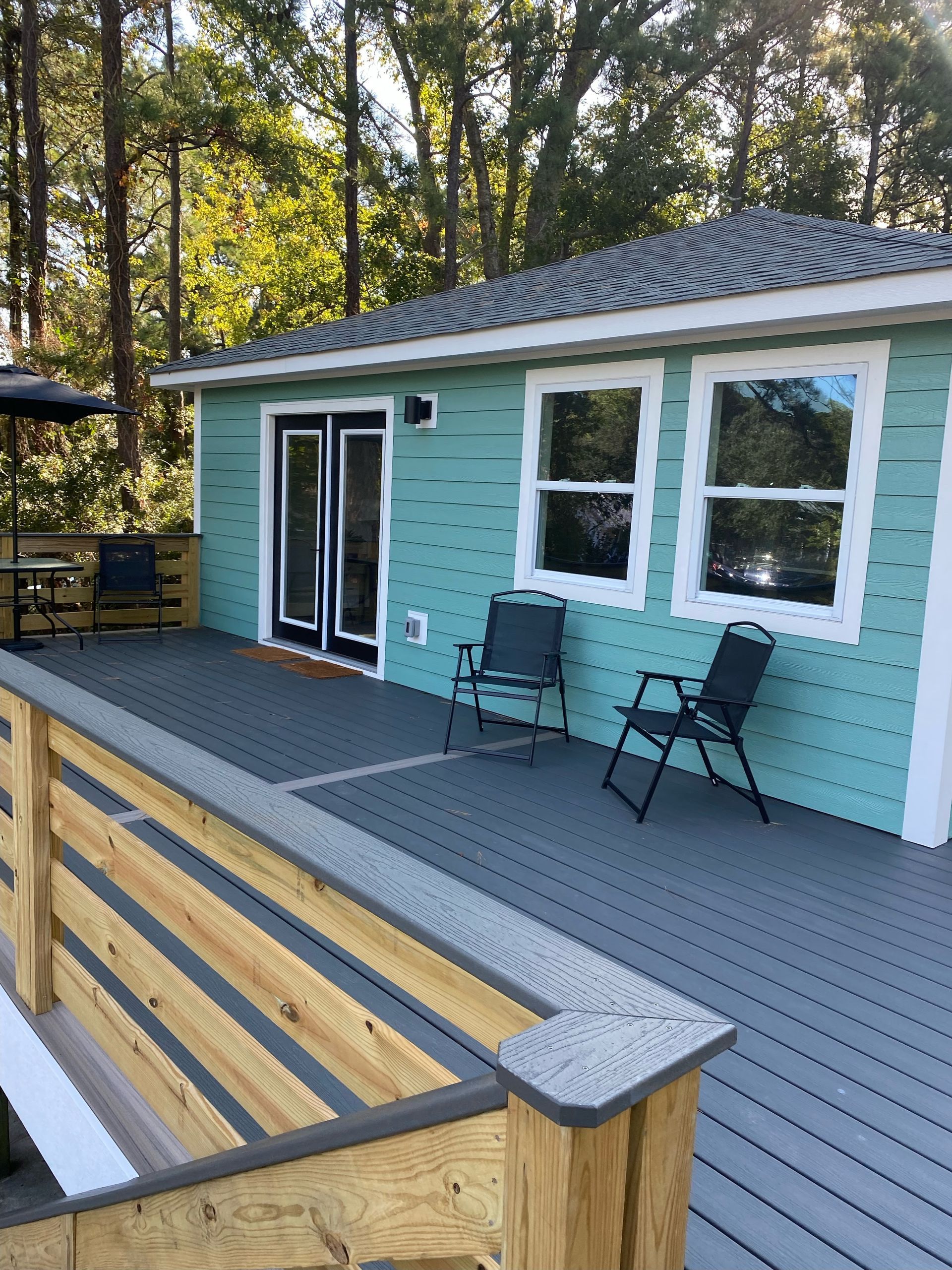 A small turquoise cottage with a grey deck, two chairs, and black double doors.