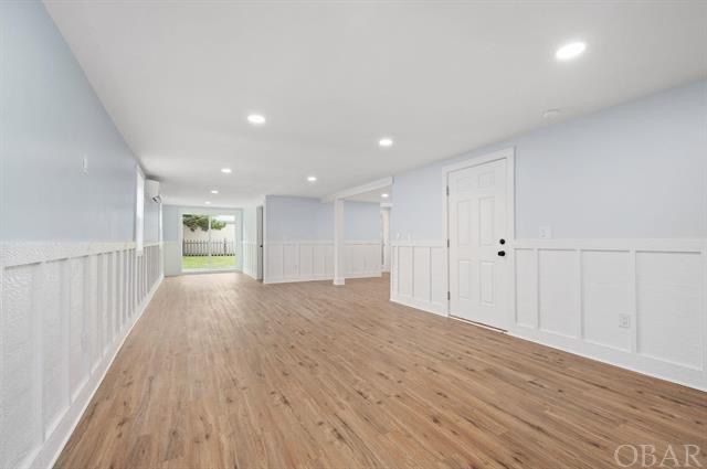 Empty room with wood floors, light blue walls, white wainscoting, and a door leading outside.