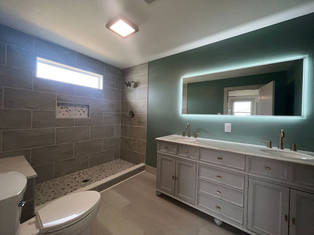 Modern bathroom with gray tile shower, green wall, double sink vanity, and a lit mirror.