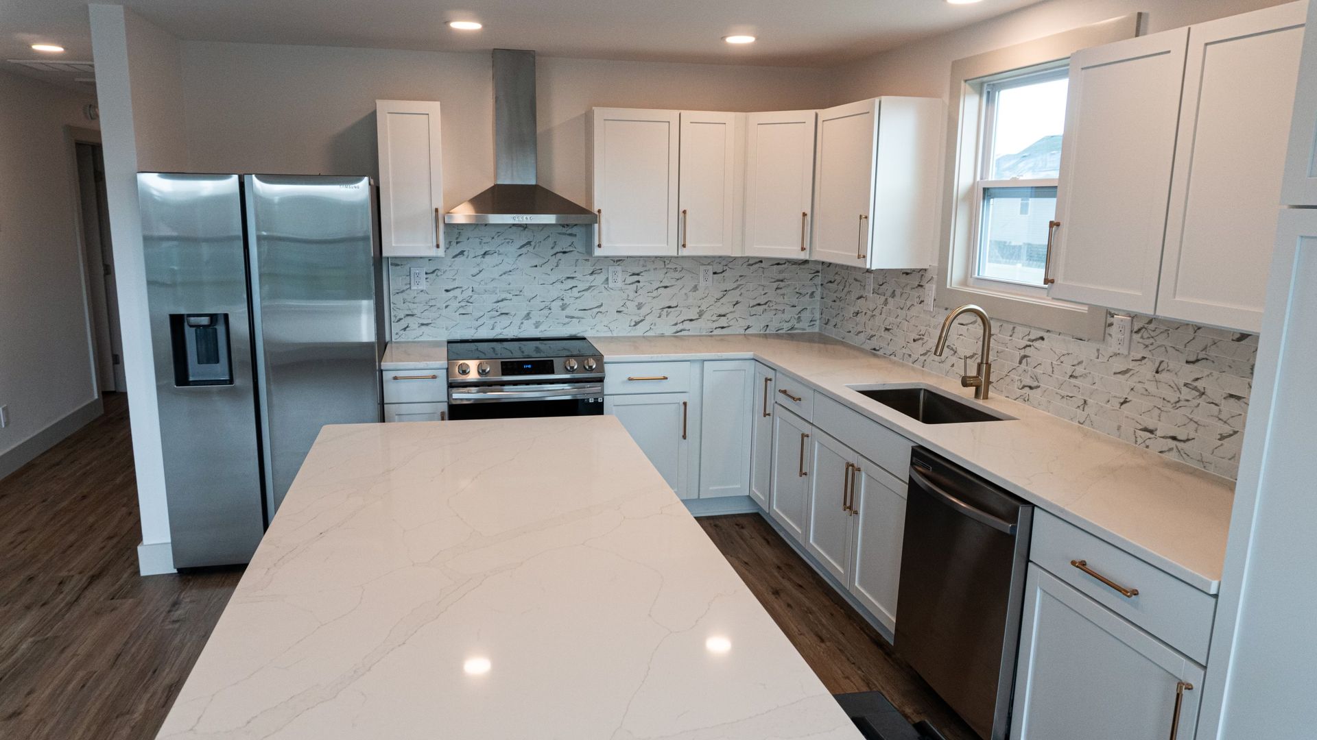 Modern white kitchen with stainless steel appliances, island, and tiled backsplash.