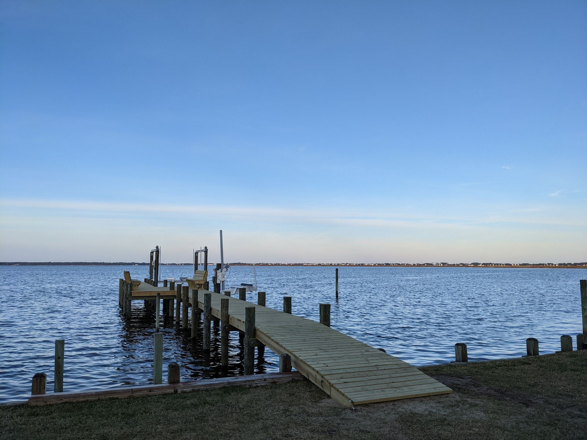 Wooden pier extending into a calm body of water, under a blue sky.
