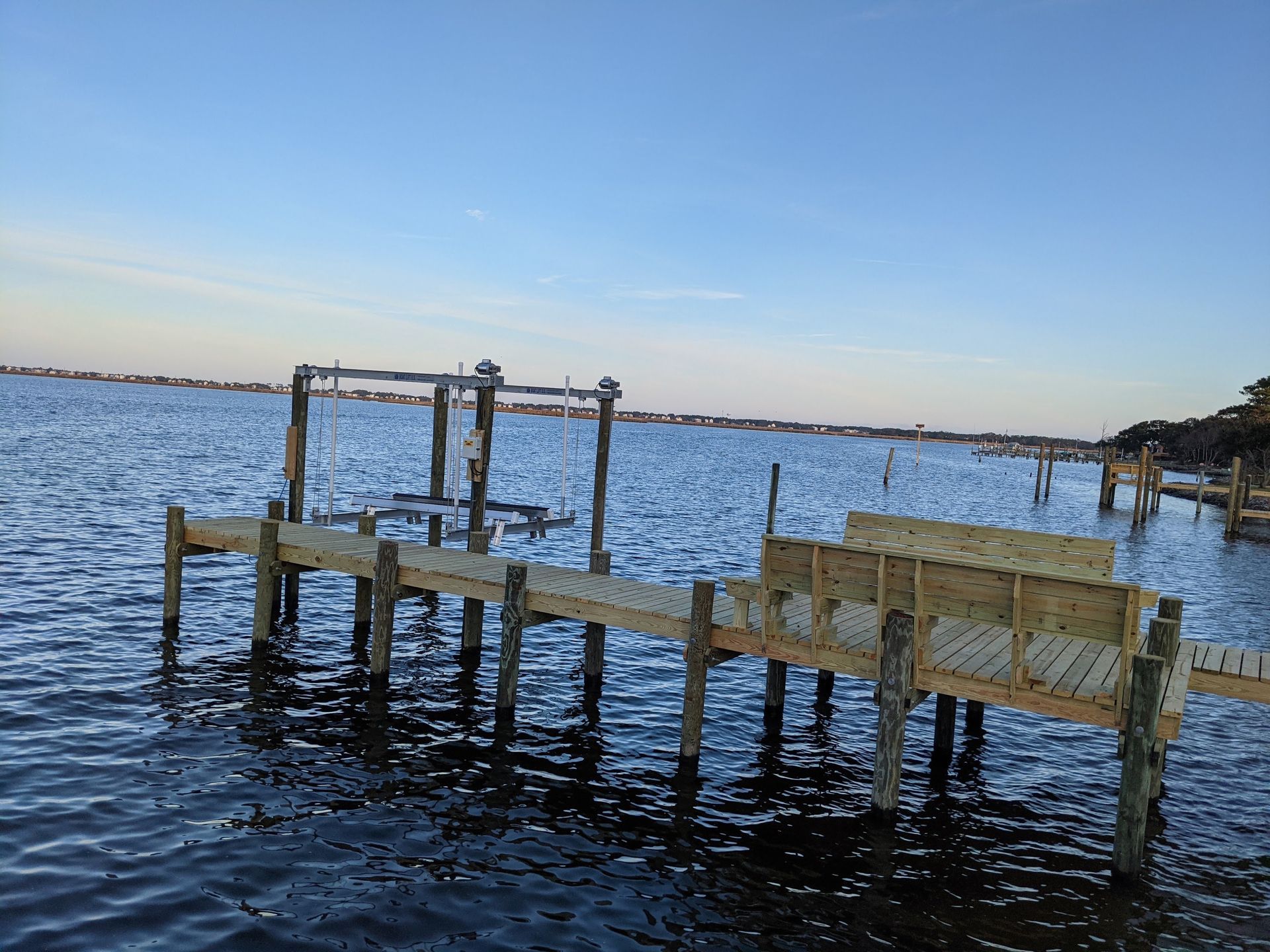 A new wooden pier extends into a body of water. Blue sky above.