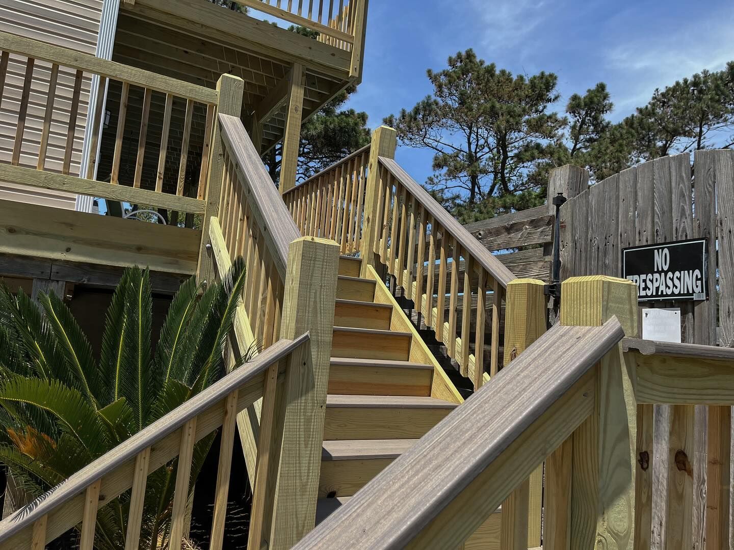 Wooden outdoor staircase leading up to a deck, with railings on both sides, sunny day.
