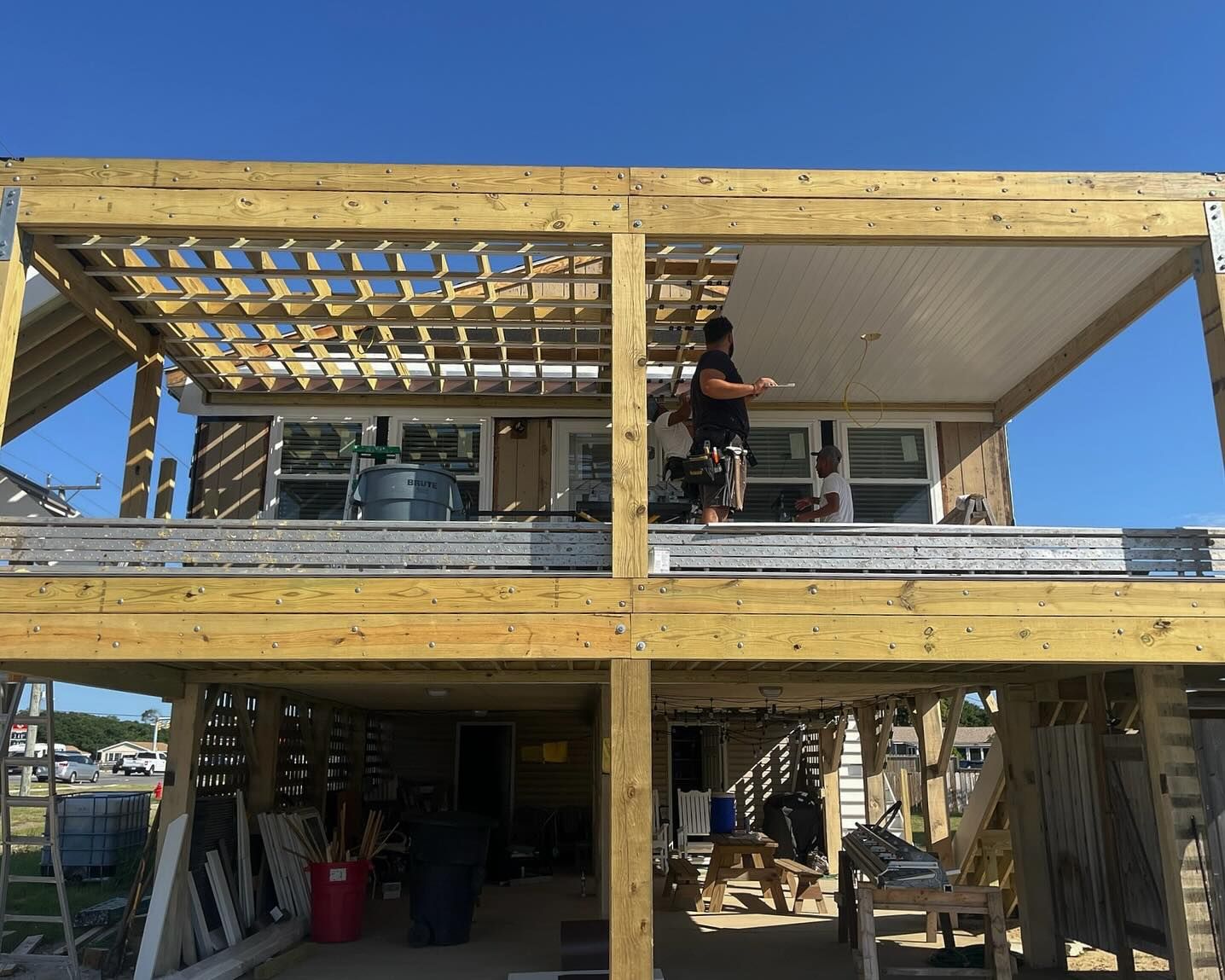 Construction worker on a two-story wooden deck; sunny day, house in the background.