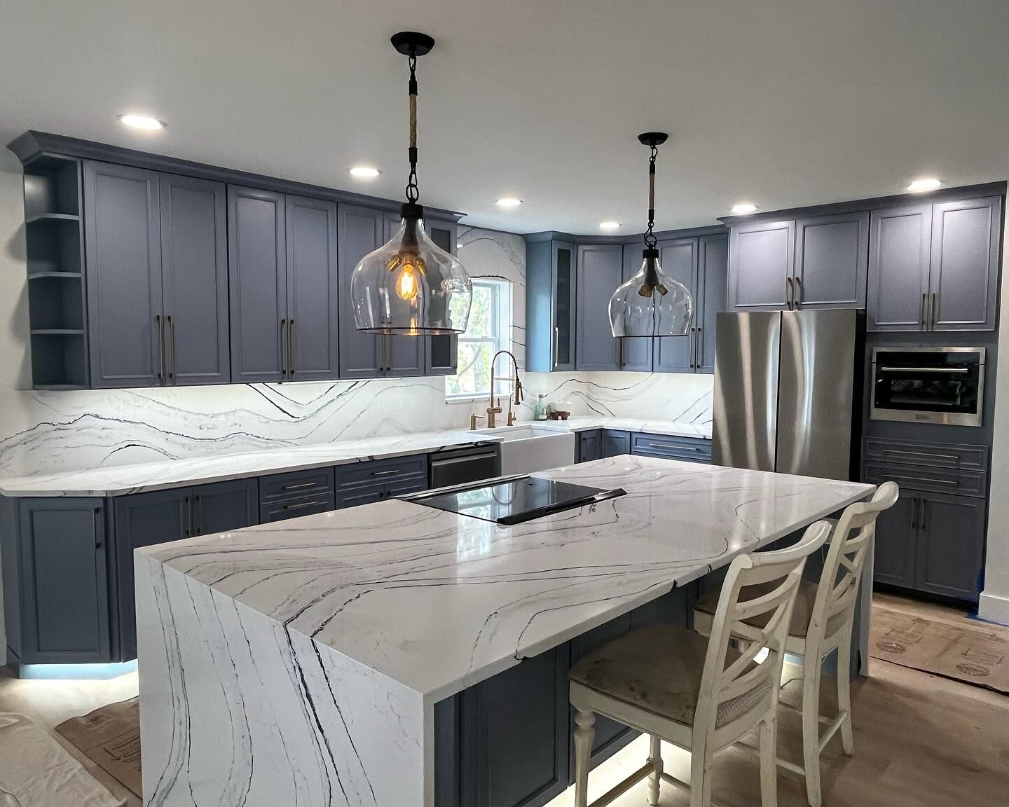 Blue and white kitchen with quartz countertops and an island with two glass pendant lights above.
