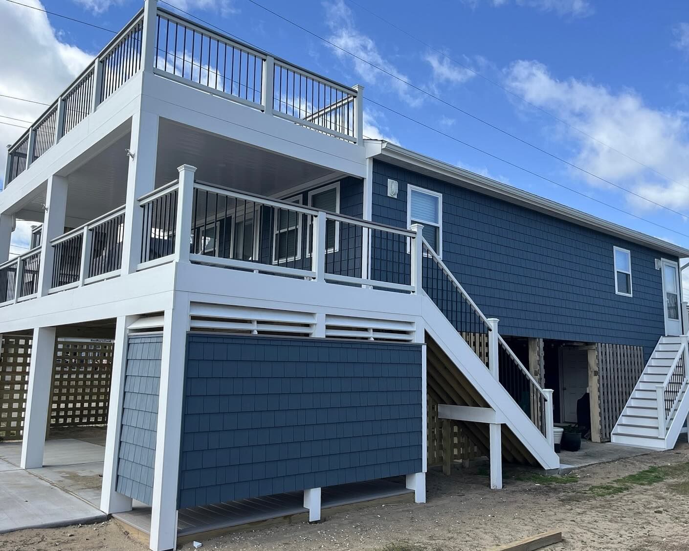 Two-story blue and white house with decks on a sunny day.