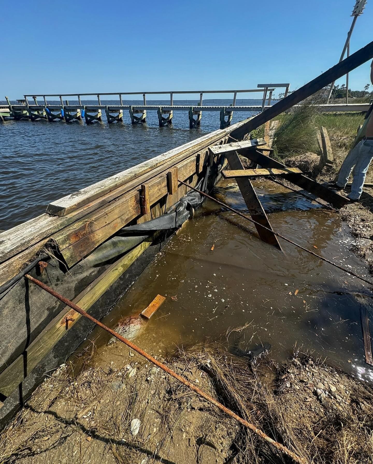 Damaged pier; water damage exposes structure. Brown wood, blue water, clear sky.