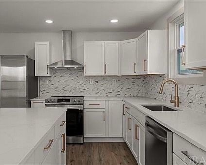Modern white kitchen with stainless steel appliances, white countertops, and copper hardware.