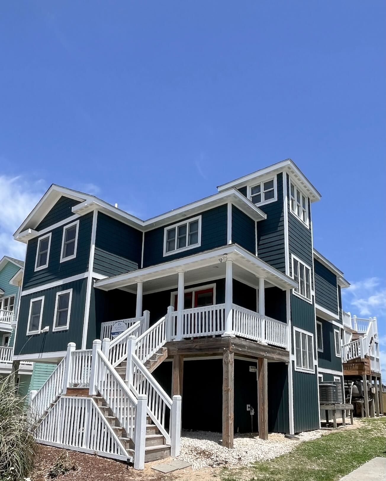 Dark blue beach house with white trim and staircase against a blue sky.