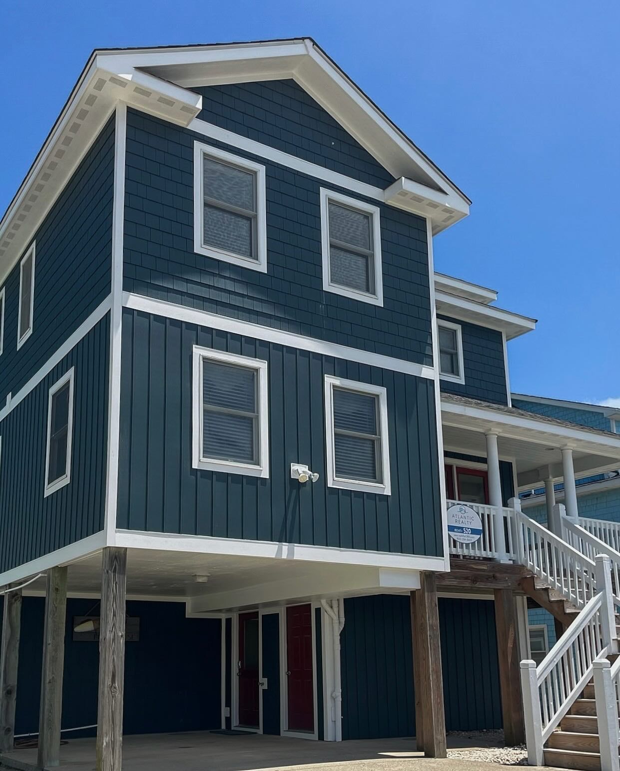 Blue two-story house on stilts with white trim, under a clear blue sky.