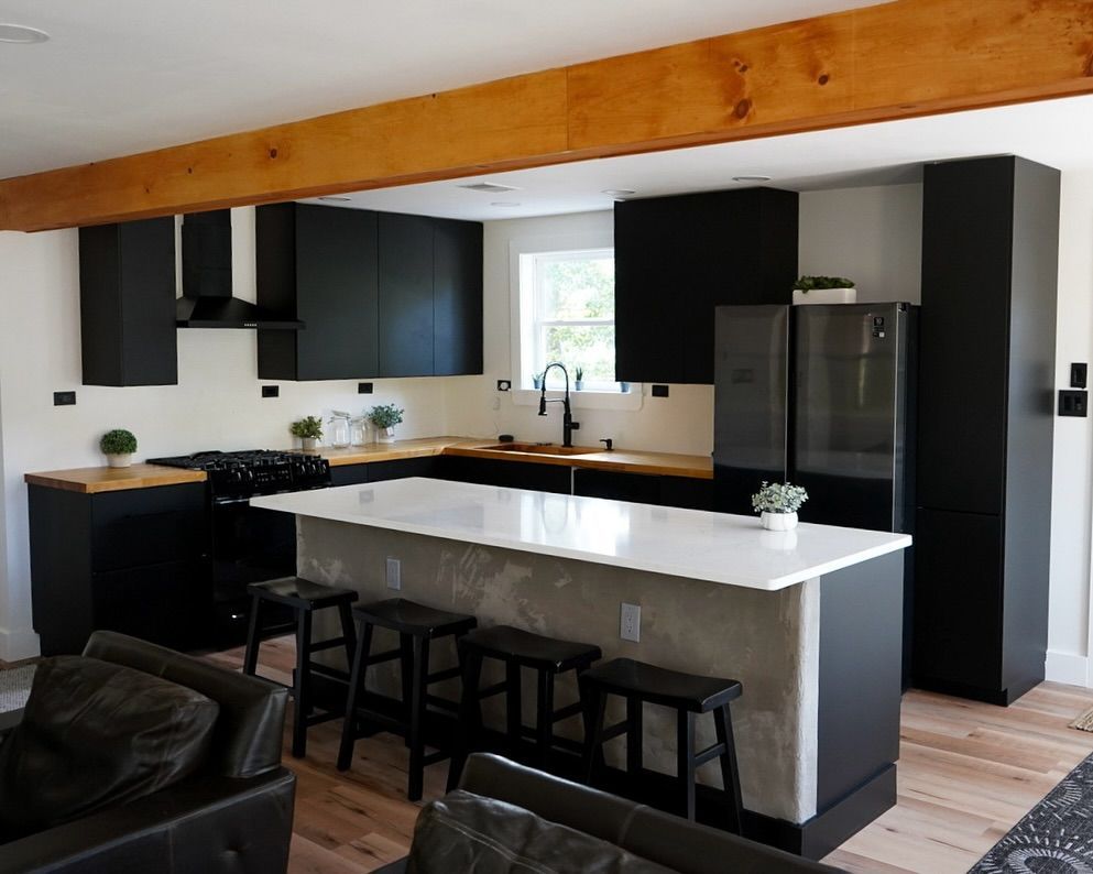 Modern kitchen with black cabinets, wood countertops, white island, and wooden beam.