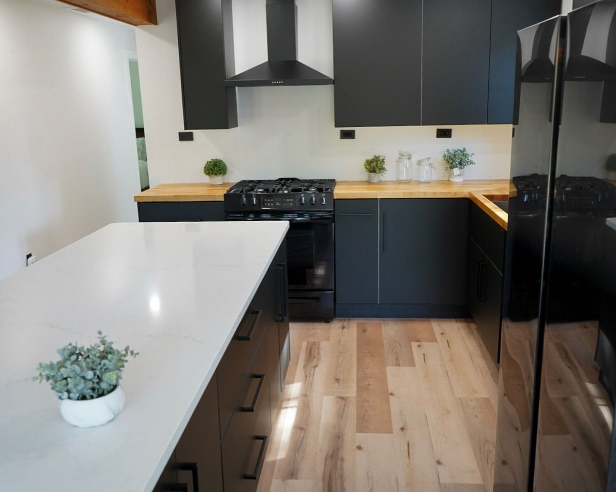 Modern kitchen with black cabinets, white island, wood countertops, and black appliances.