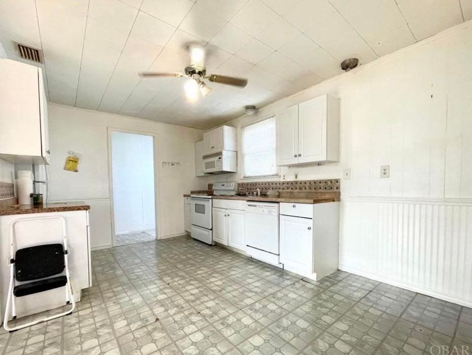 White kitchen with white cabinets, stove, and ceiling fan. Gray tiled floor.