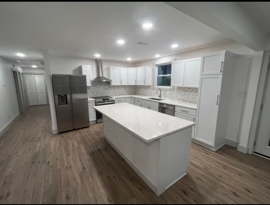 Modern white kitchen with island, stainless steel appliances, and light wood floors.
