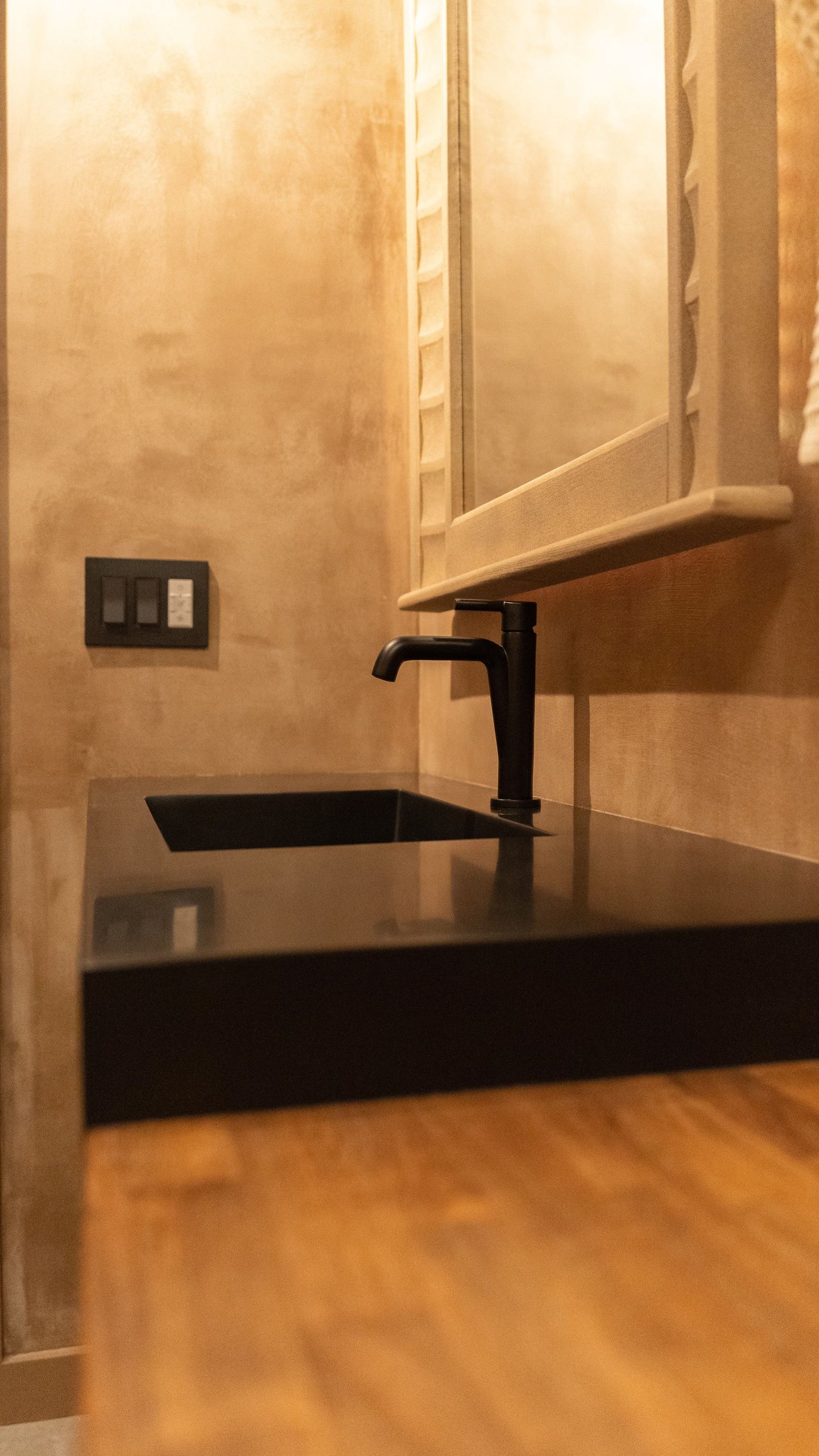 Black faucet over a dark sink on a dark countertop in a bathroom, with a mirror.