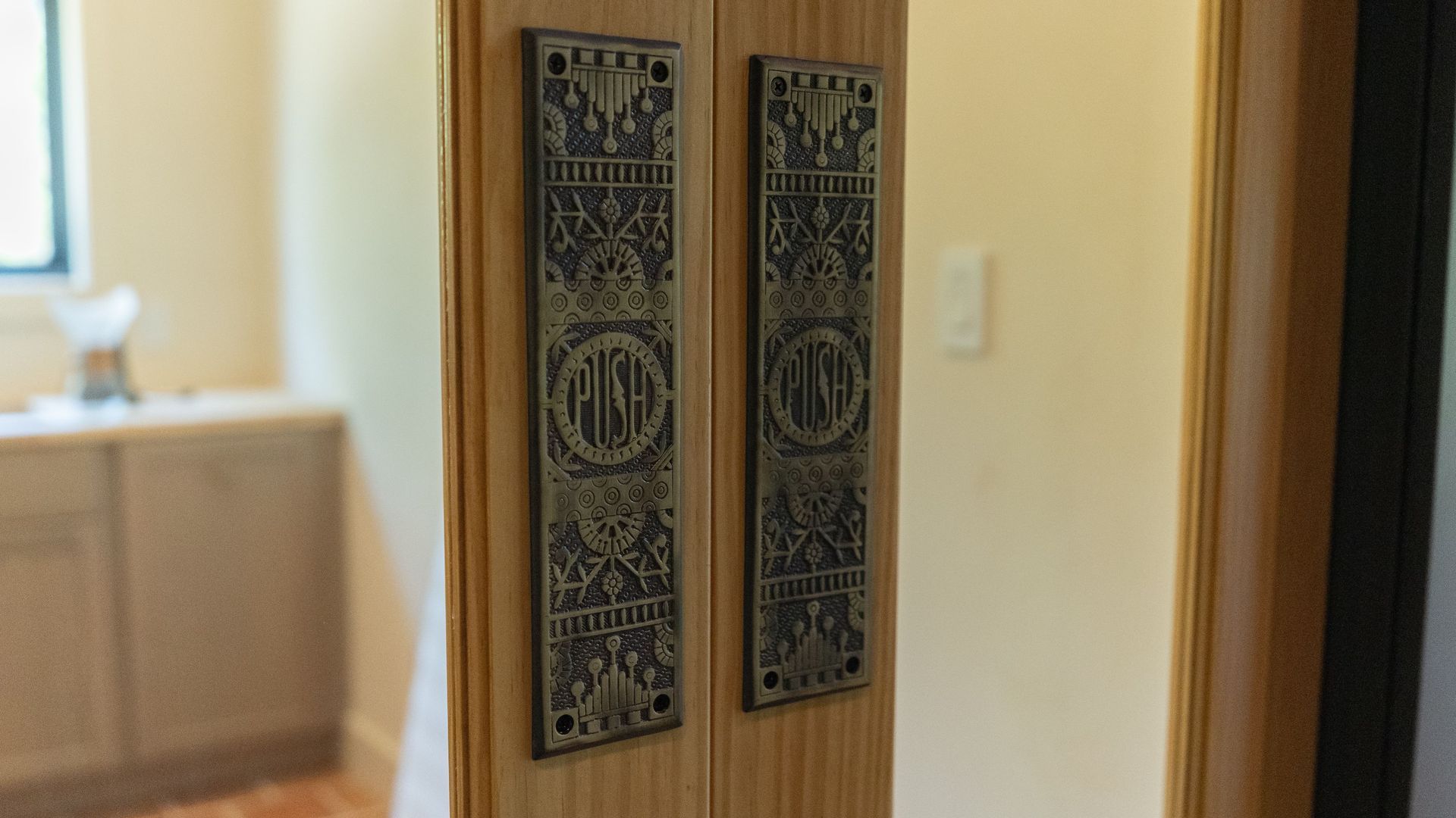 Two decorative, bronze-toned door handles with ornate designs on wooden door.