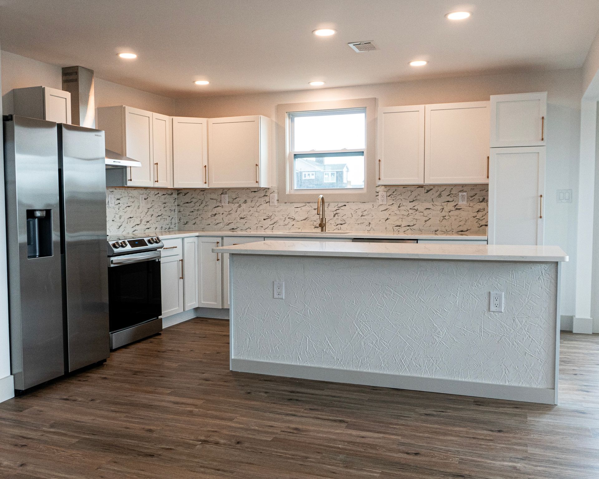 Modern white kitchen with stainless steel appliances, light countertops, and a large island.