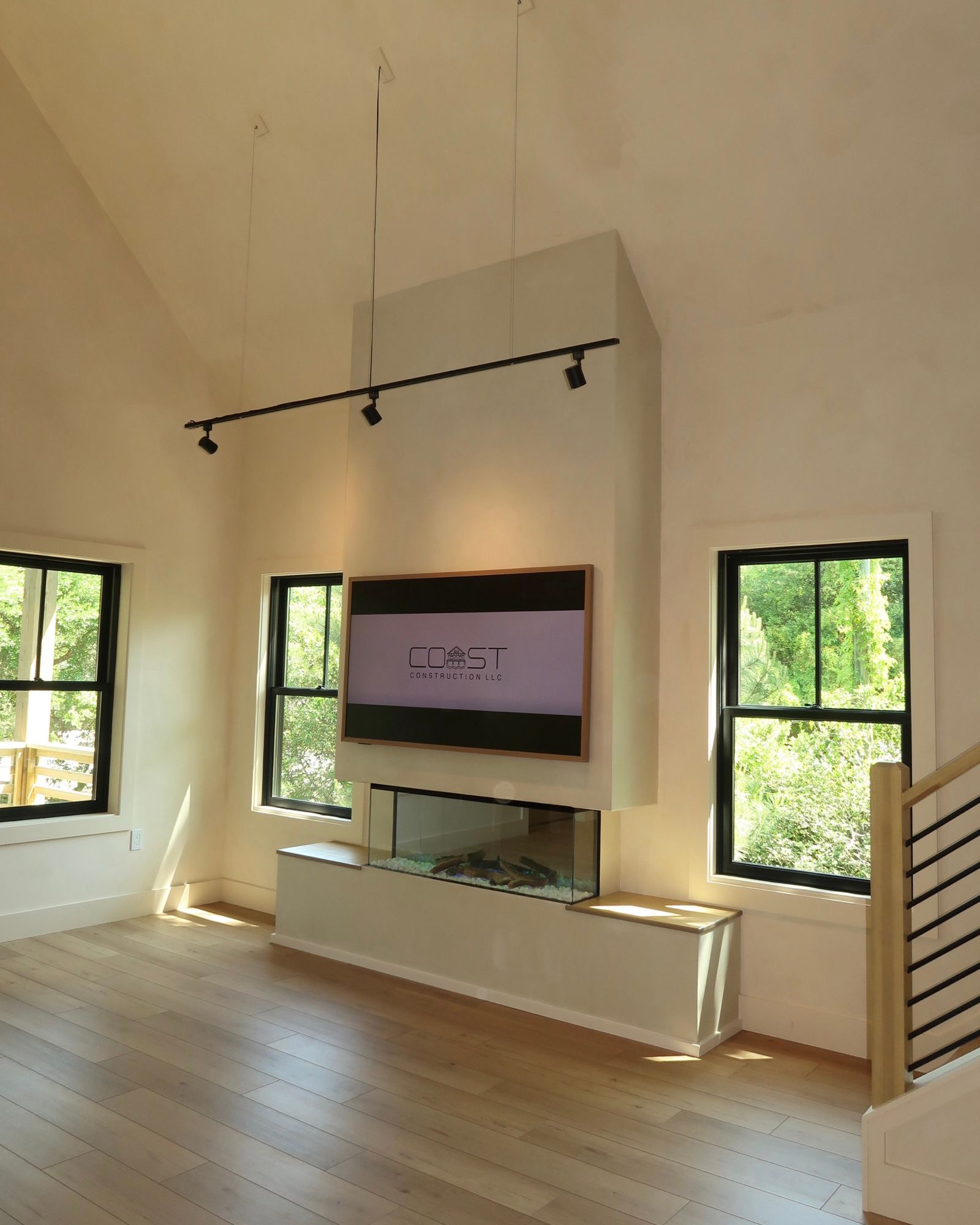 Living room with tall fireplace and TV, windows, and hardwood floors.