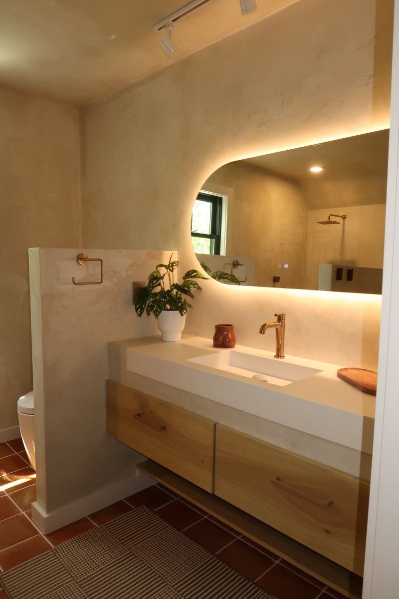 Modern bathroom with floating wood vanity, backlit mirror, and terracotta floors.