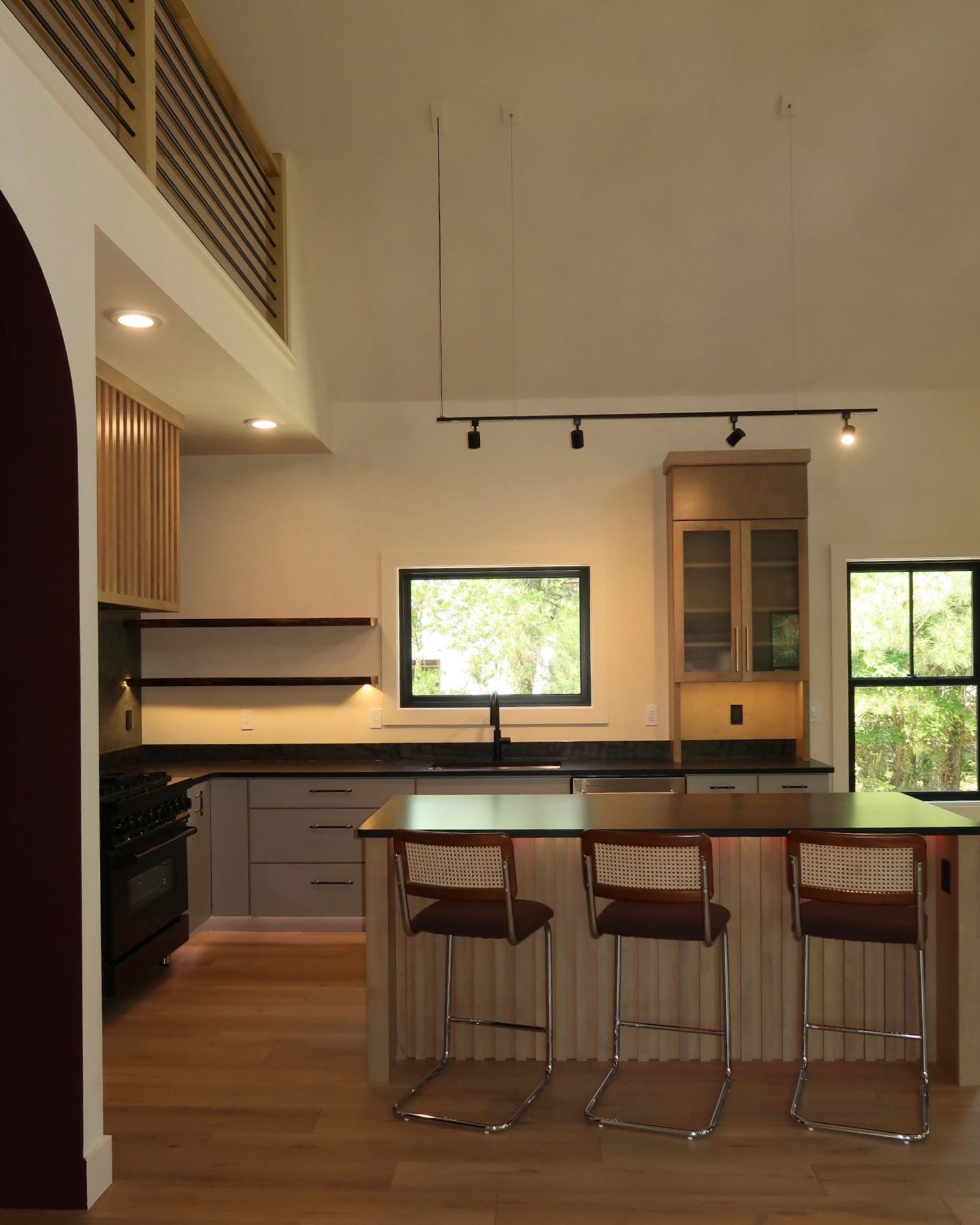 Modern kitchen with island, grey cabinets, light wood floors, and three bar stools.
