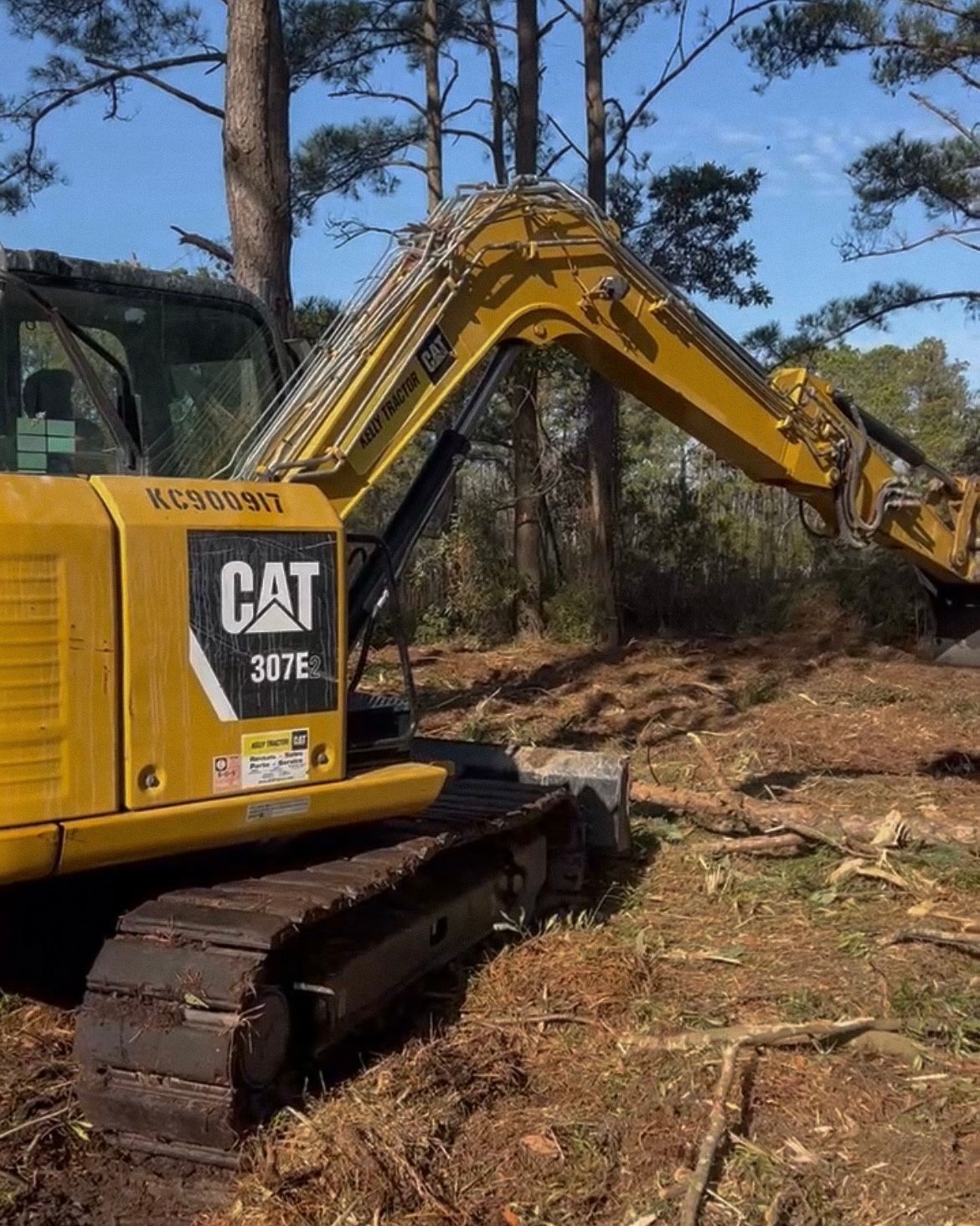 Yellow CAT 336E L excavator clearing land, trees in background.