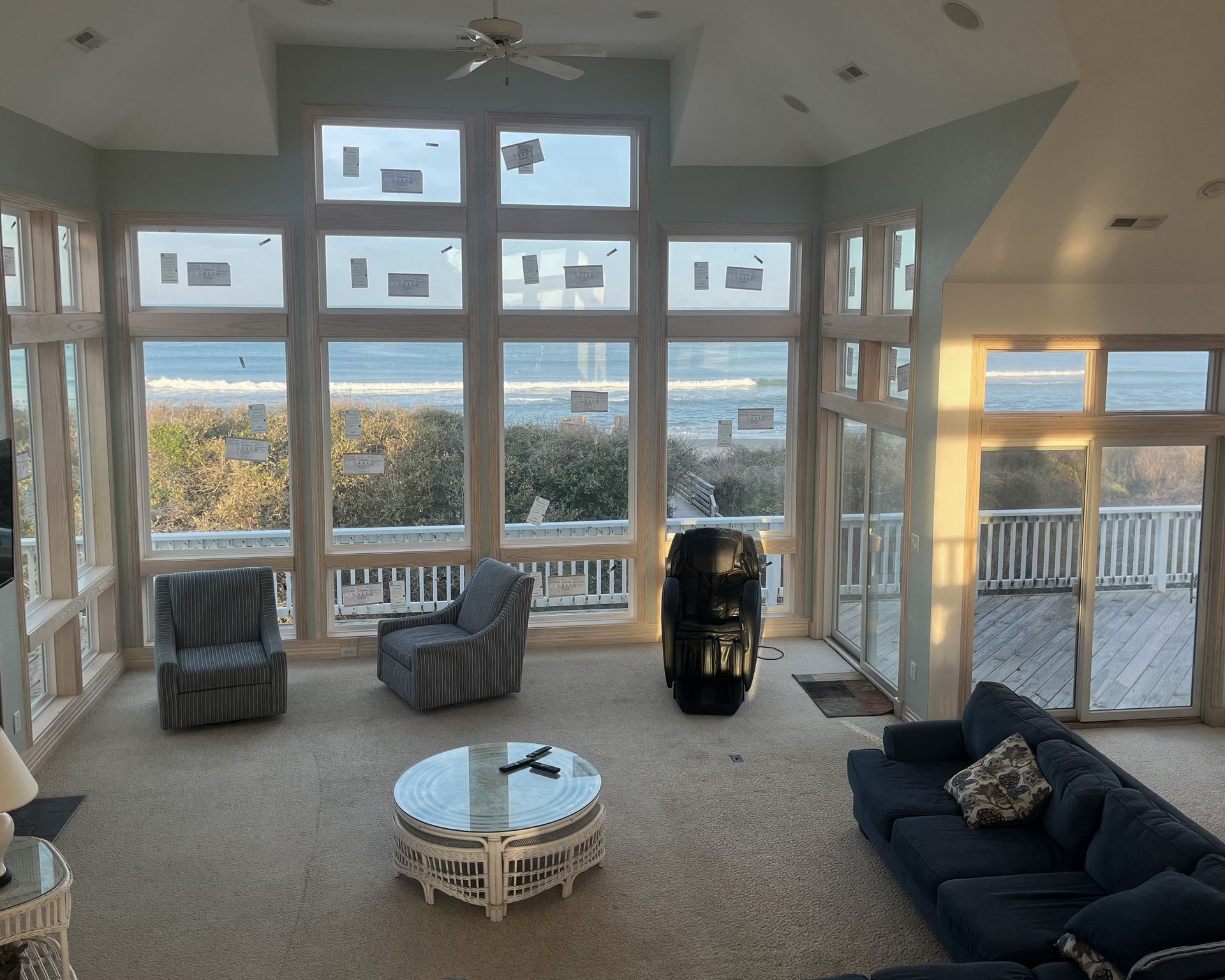 Living room with large windows overlooking the ocean. Furnishings include chairs, a sofa, and a coffee table.