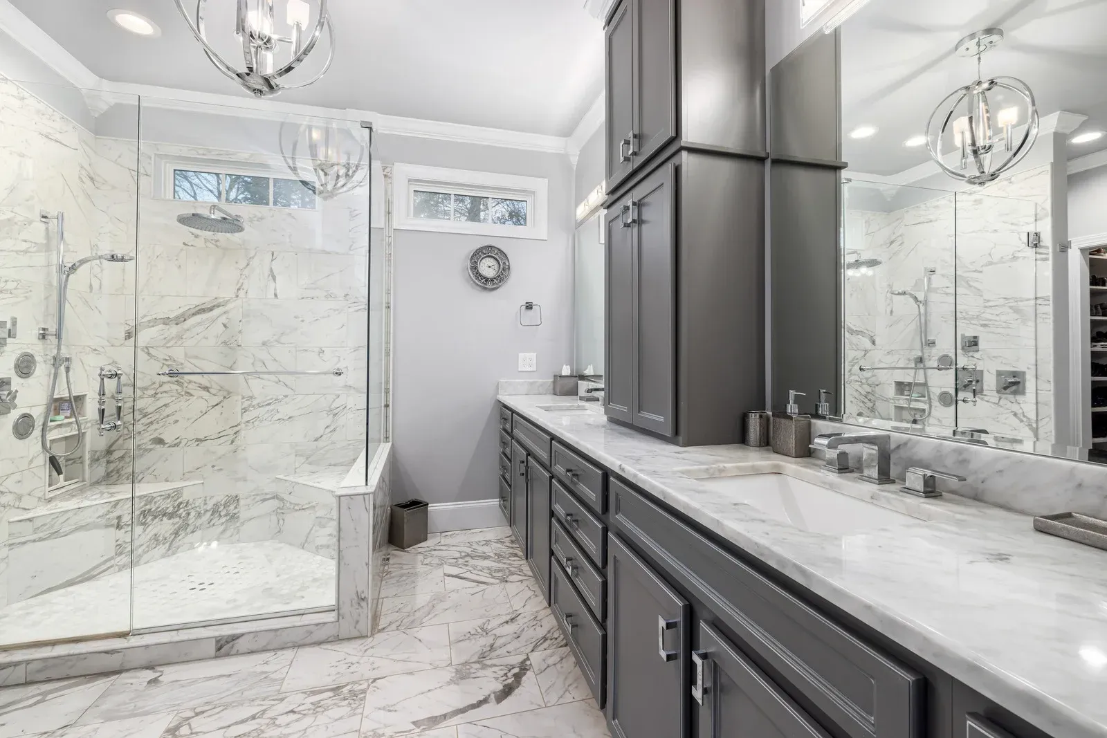 Gray and white luxury bathroom with shower, vanity, cabinets, and marble surfaces.