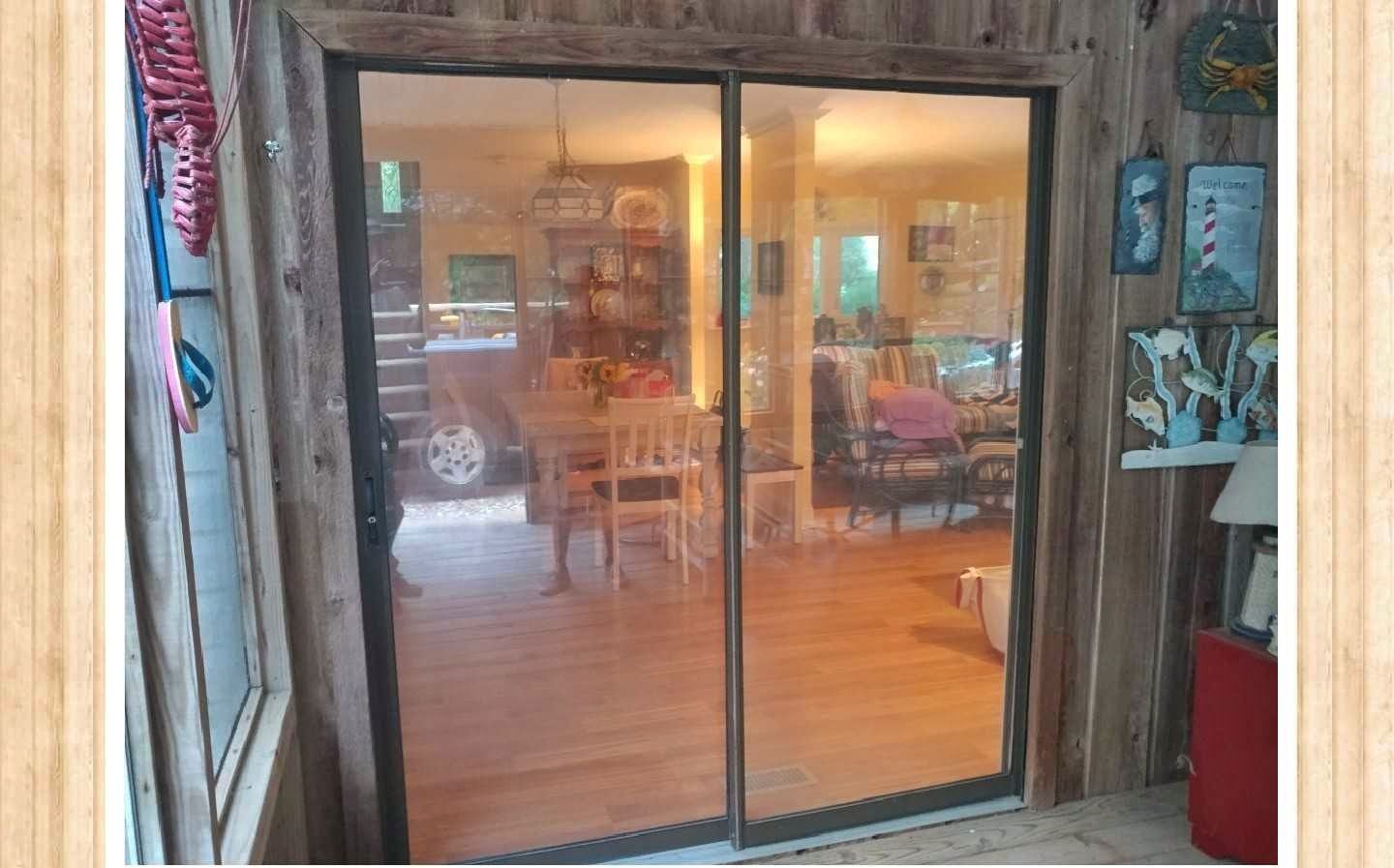 Sliding glass doors reflect a dining room with a table, chairs, and decorations. Rustic wood siding surrounds the doors.